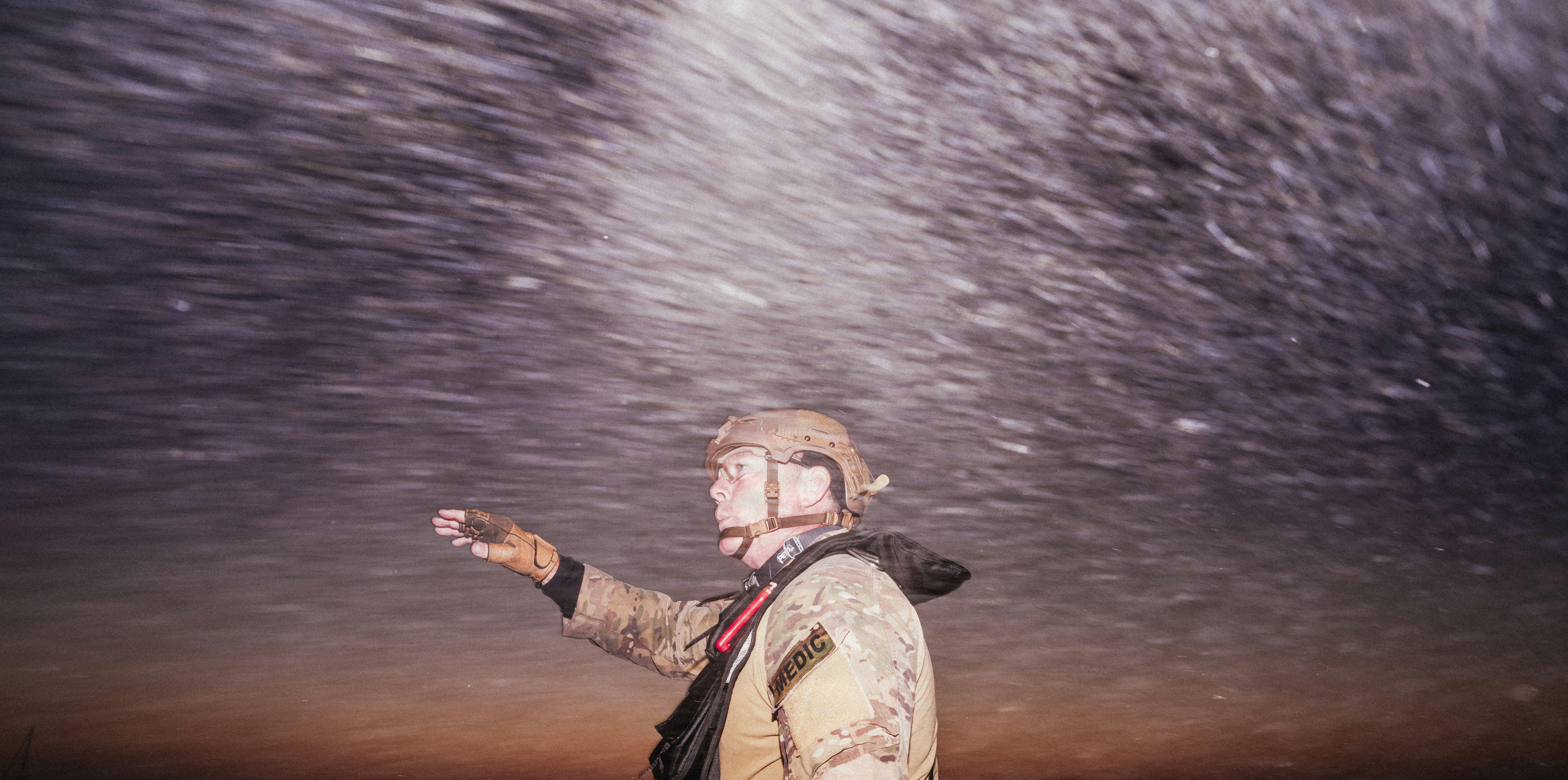 A person in a tactical helmet and uniform pointing into a dark sky