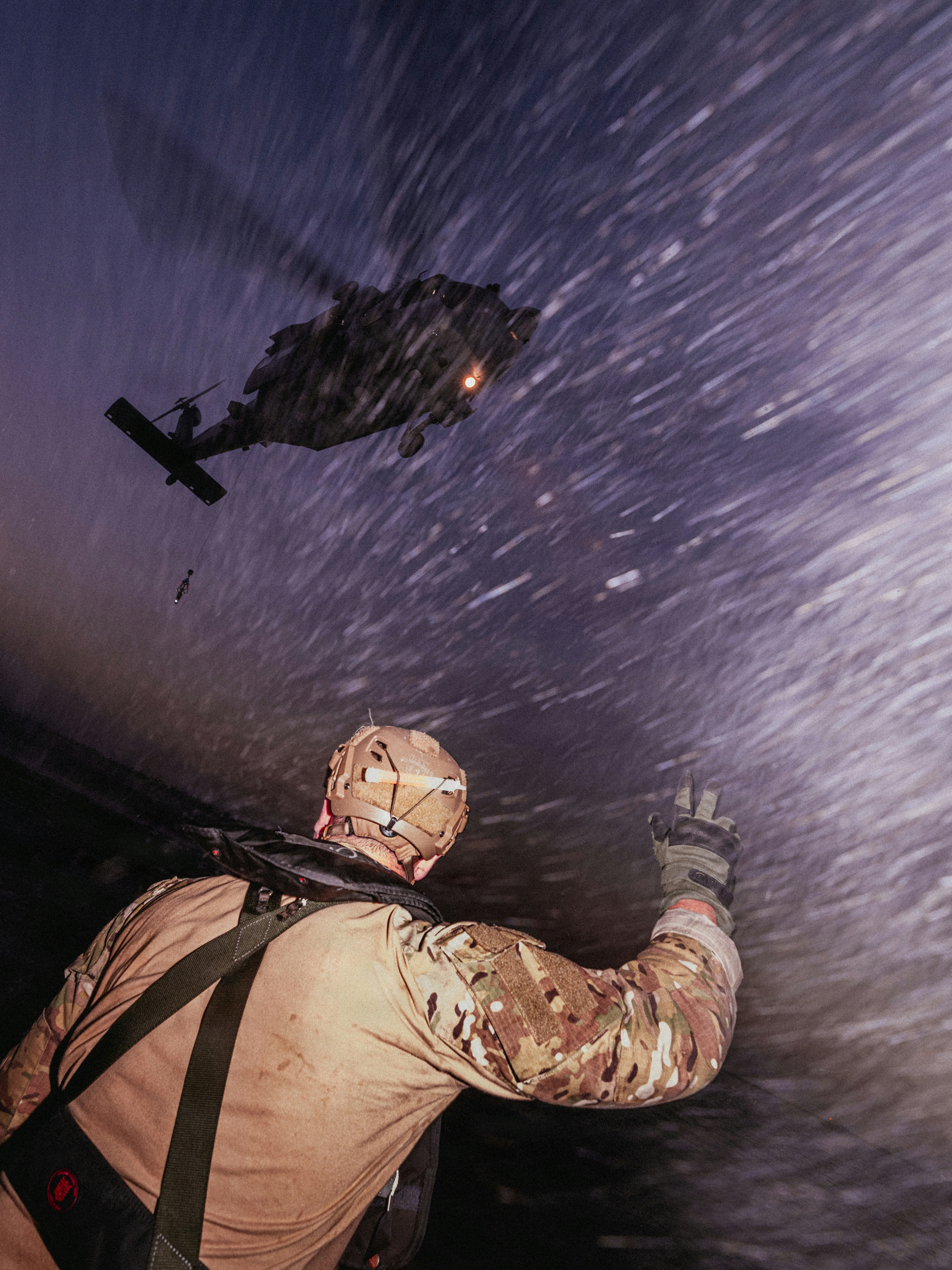 A person in camouflage gear signaling a helicopter hovering in a snowstorm