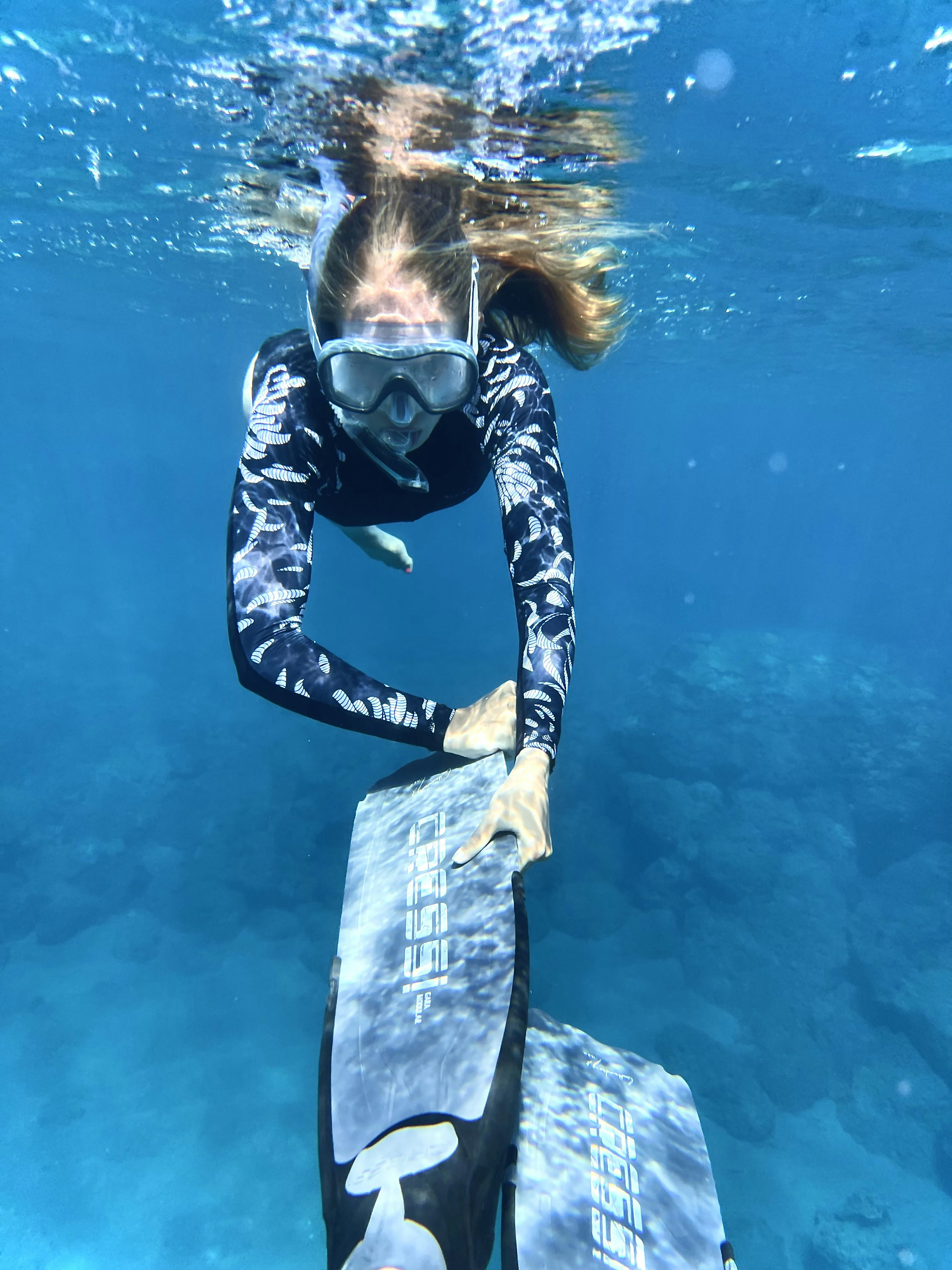 A woman snorkeling in blue water wearing a patterned wetsuit and diving mask