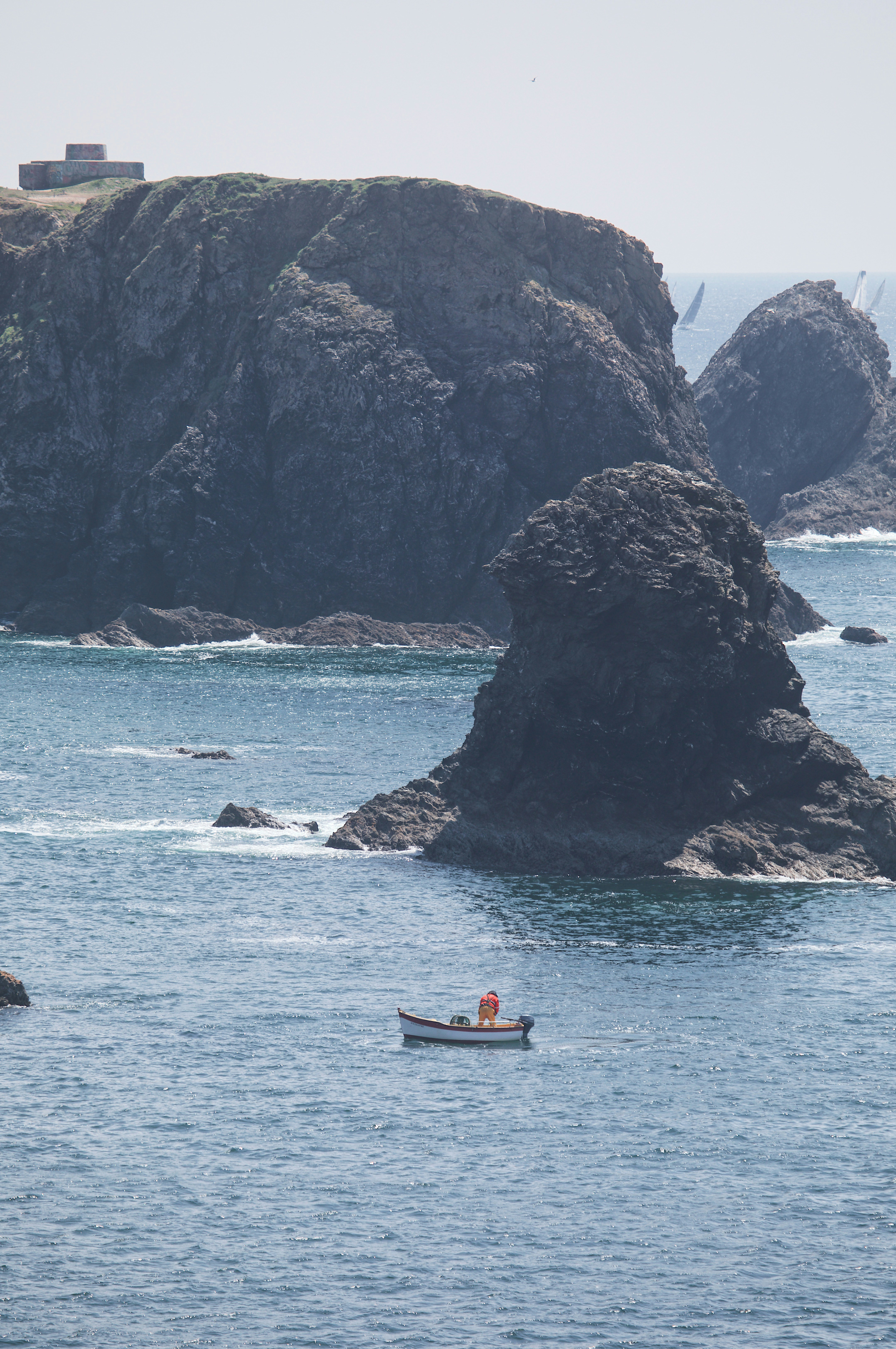 A person in a small boat near large dark rocky cliffs in the ocean