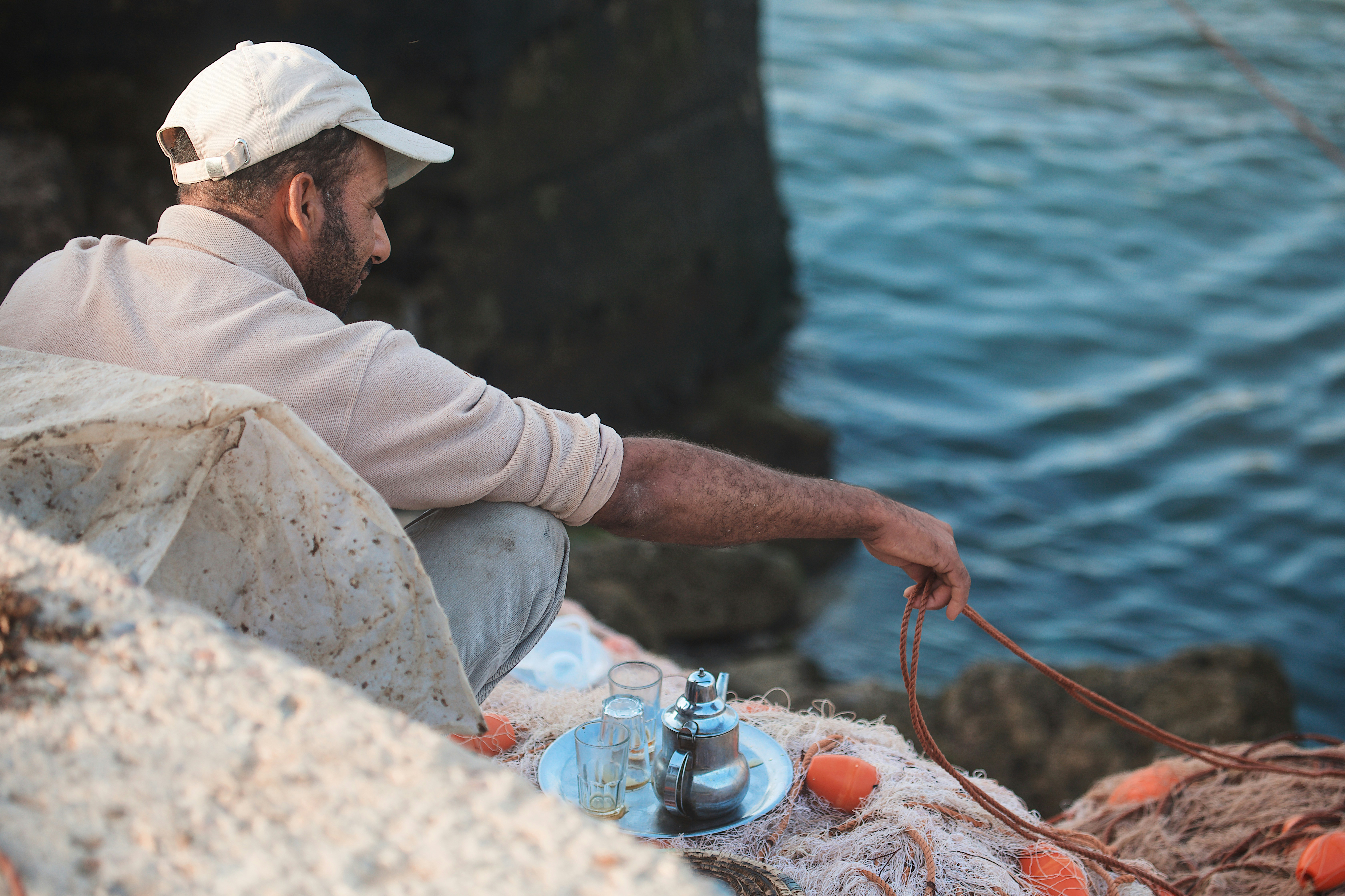 A man in a white cap holding a rope by the sea with tea