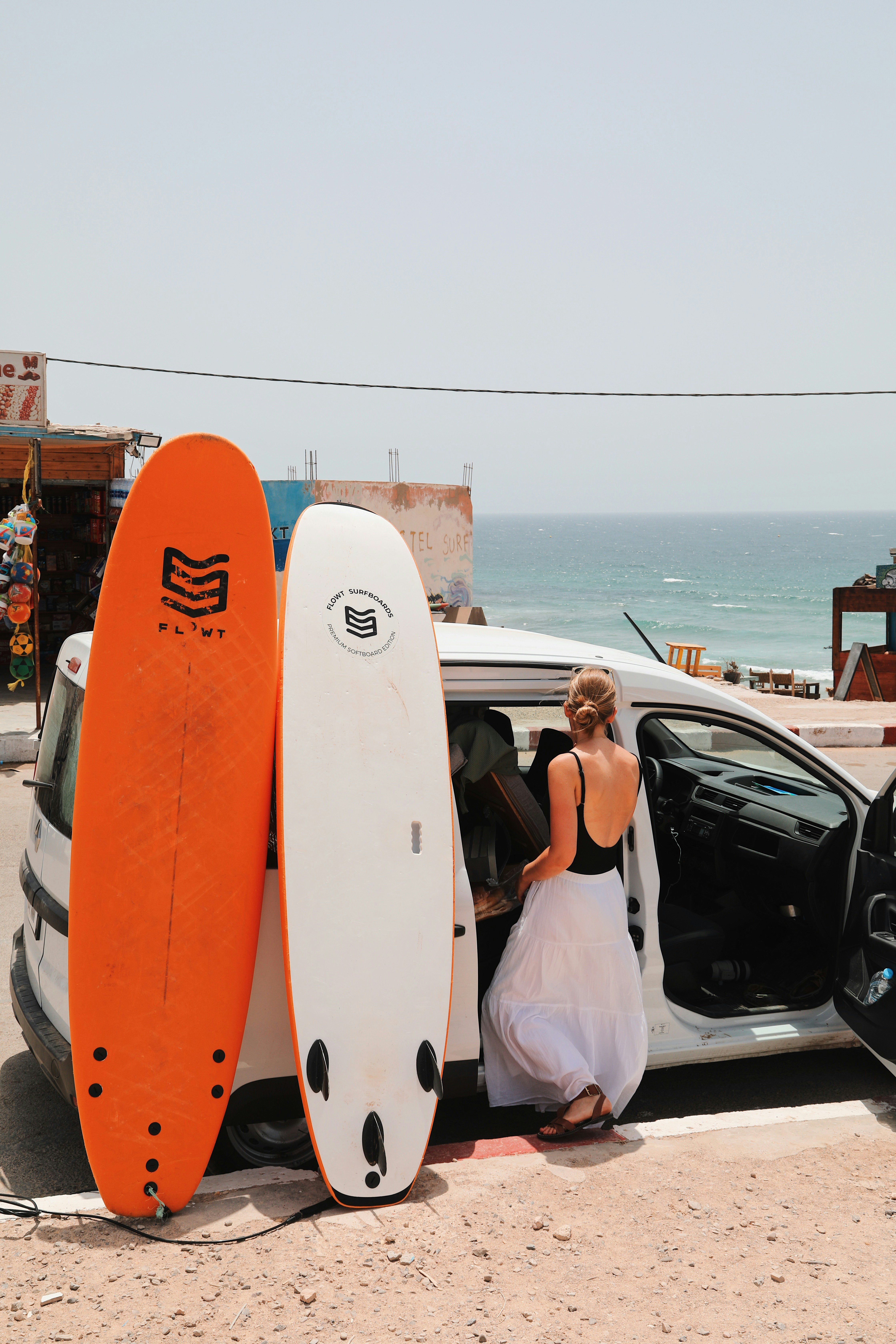 A woman in a black top and white skirt loading a white van with surfboards