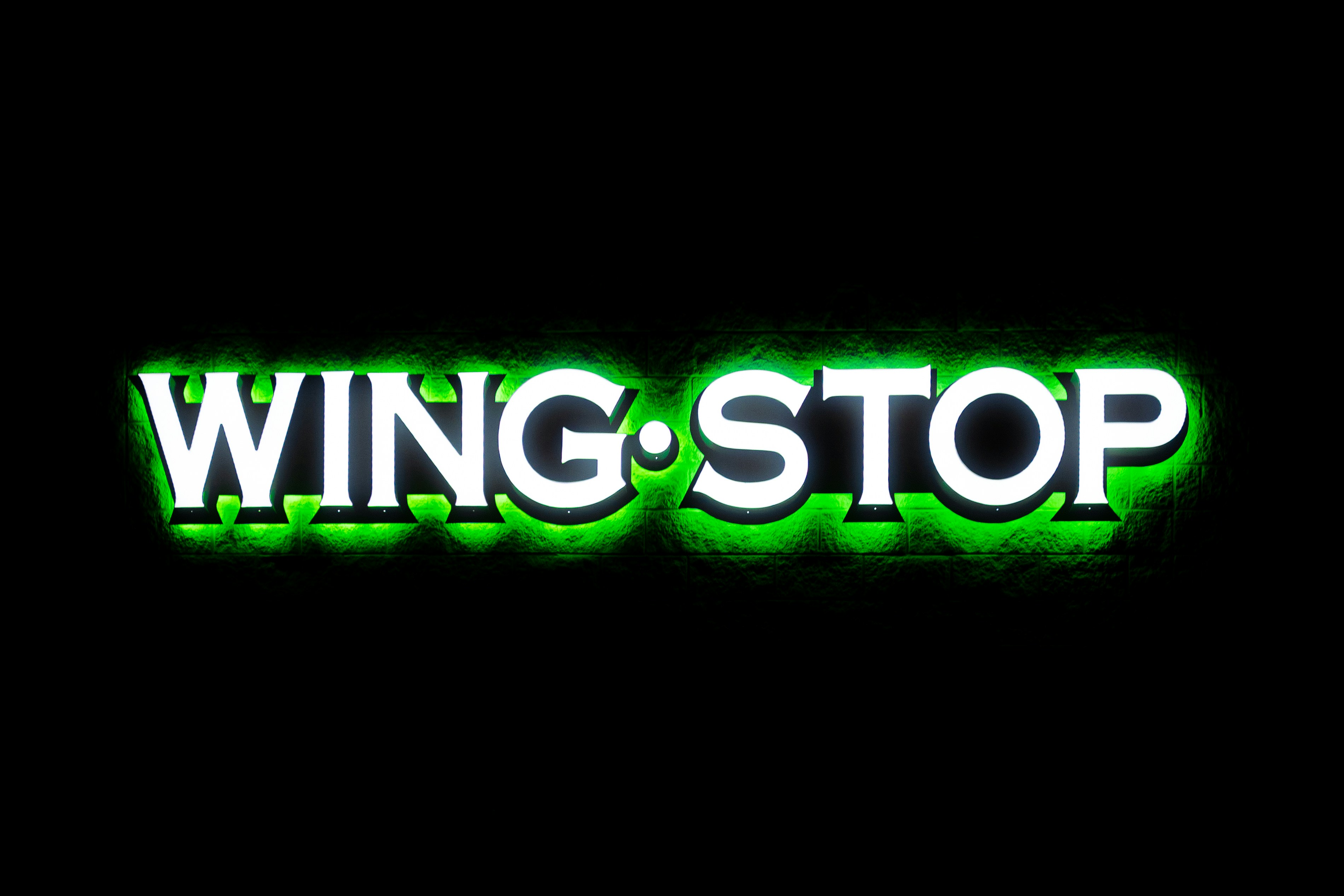 Ein leuchtend weiß-grünes Wingstop-Schild ist an einer dunkel strukturierten Wand montiert