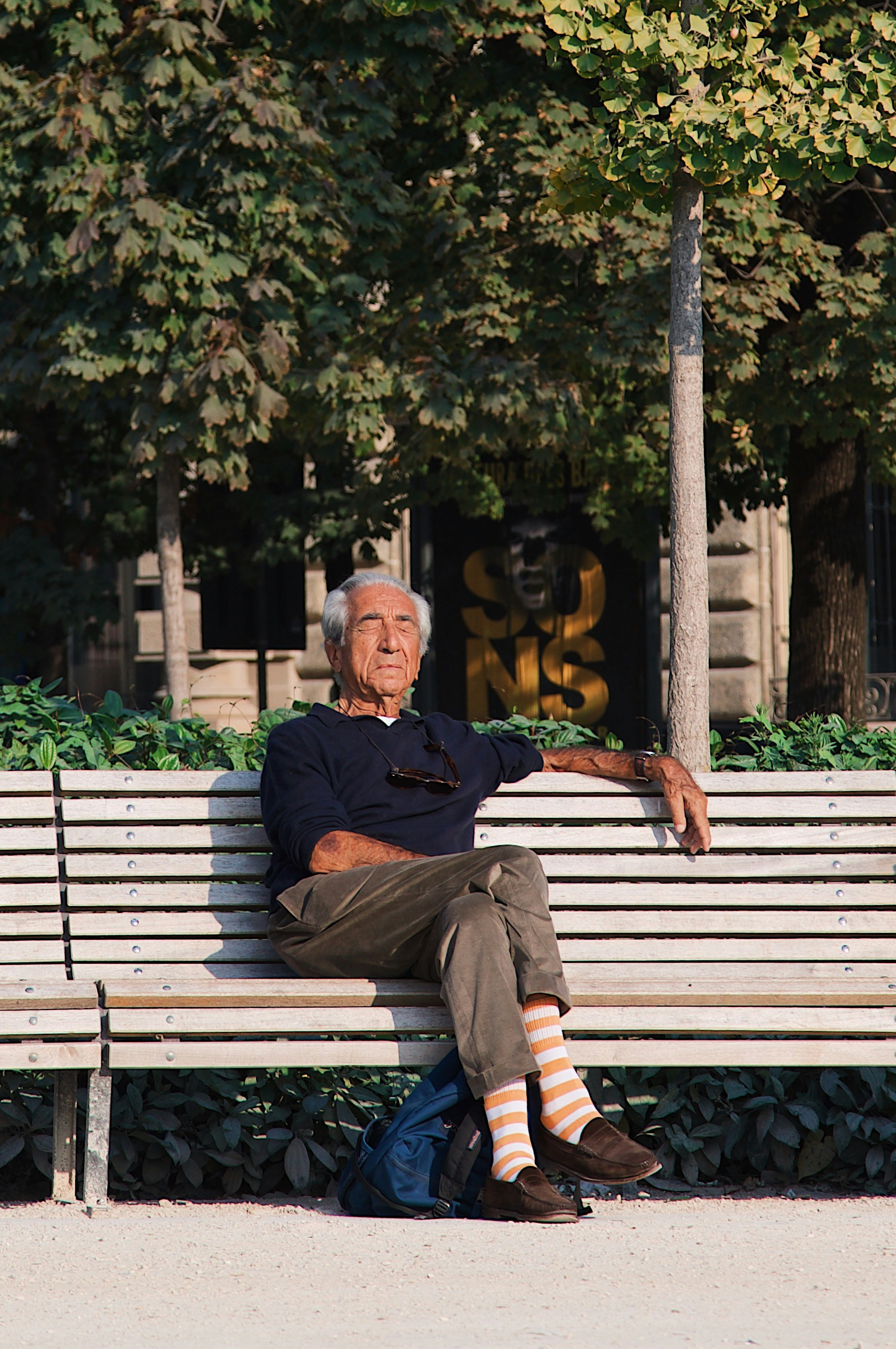 An elderly man with grey hair resting on a wooden park bench