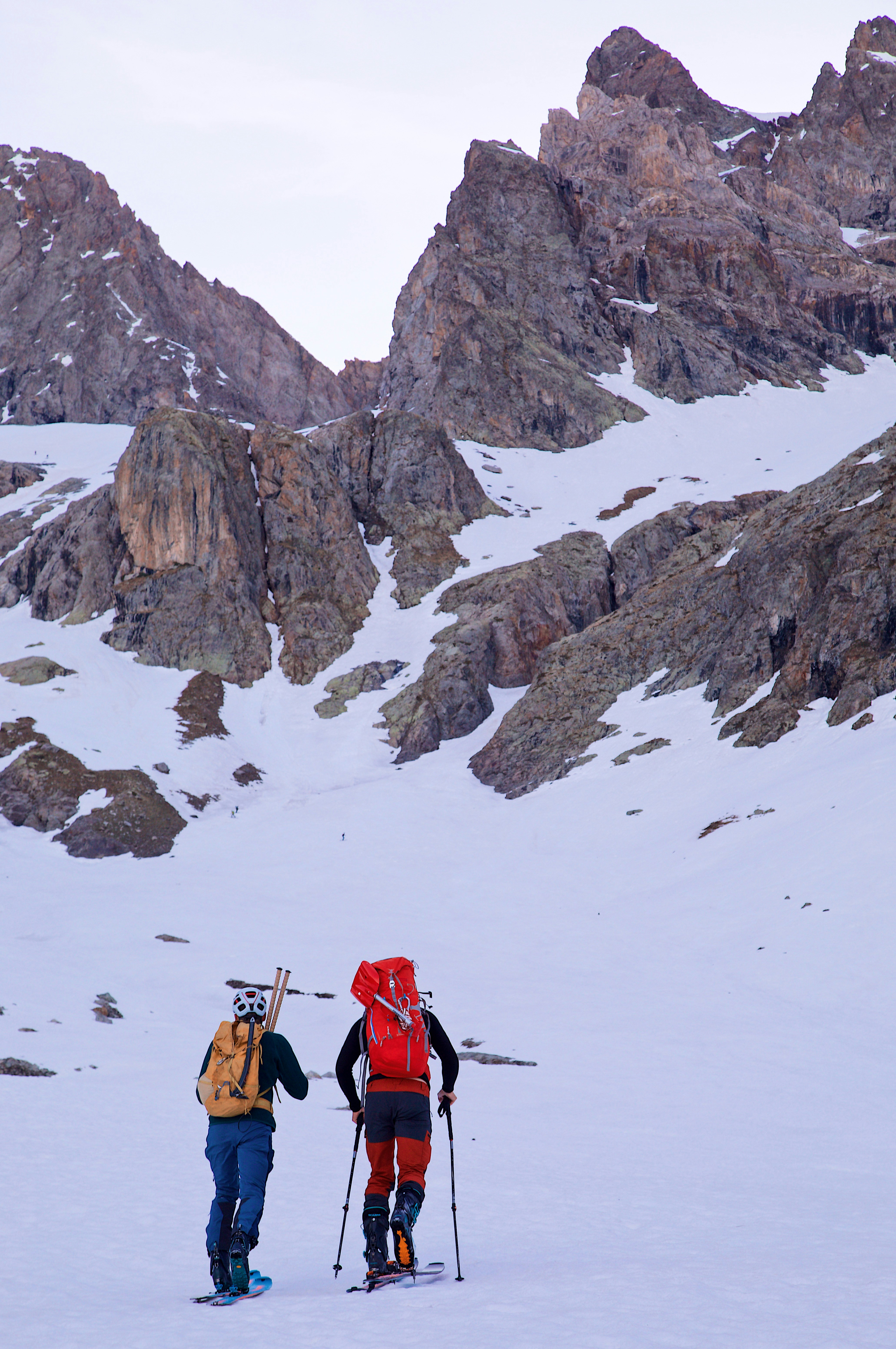 Two people ski touring up a snowy mountain slope toward a rocky peak