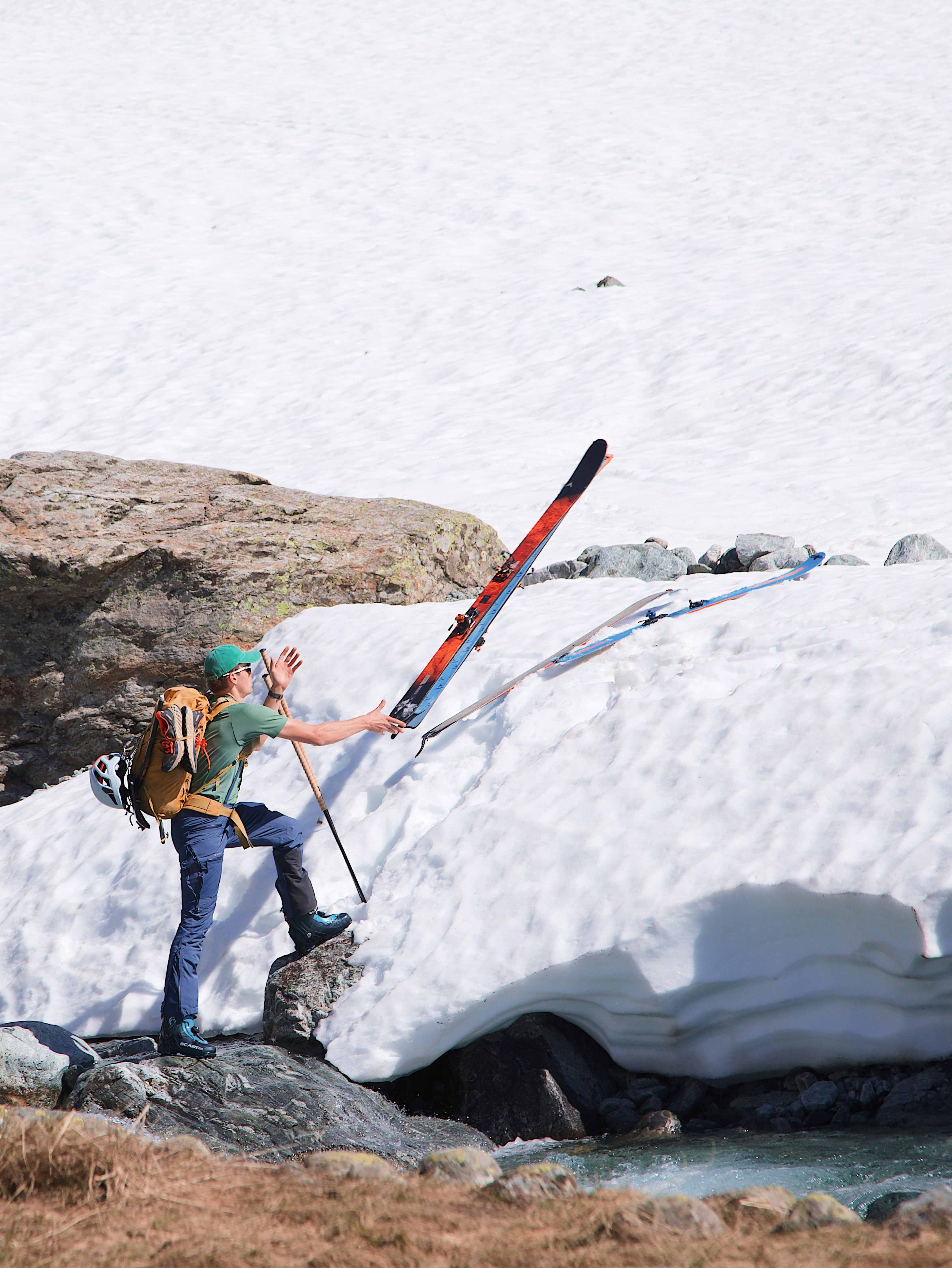 A person with a backpack reaching for skis on a snowy slope