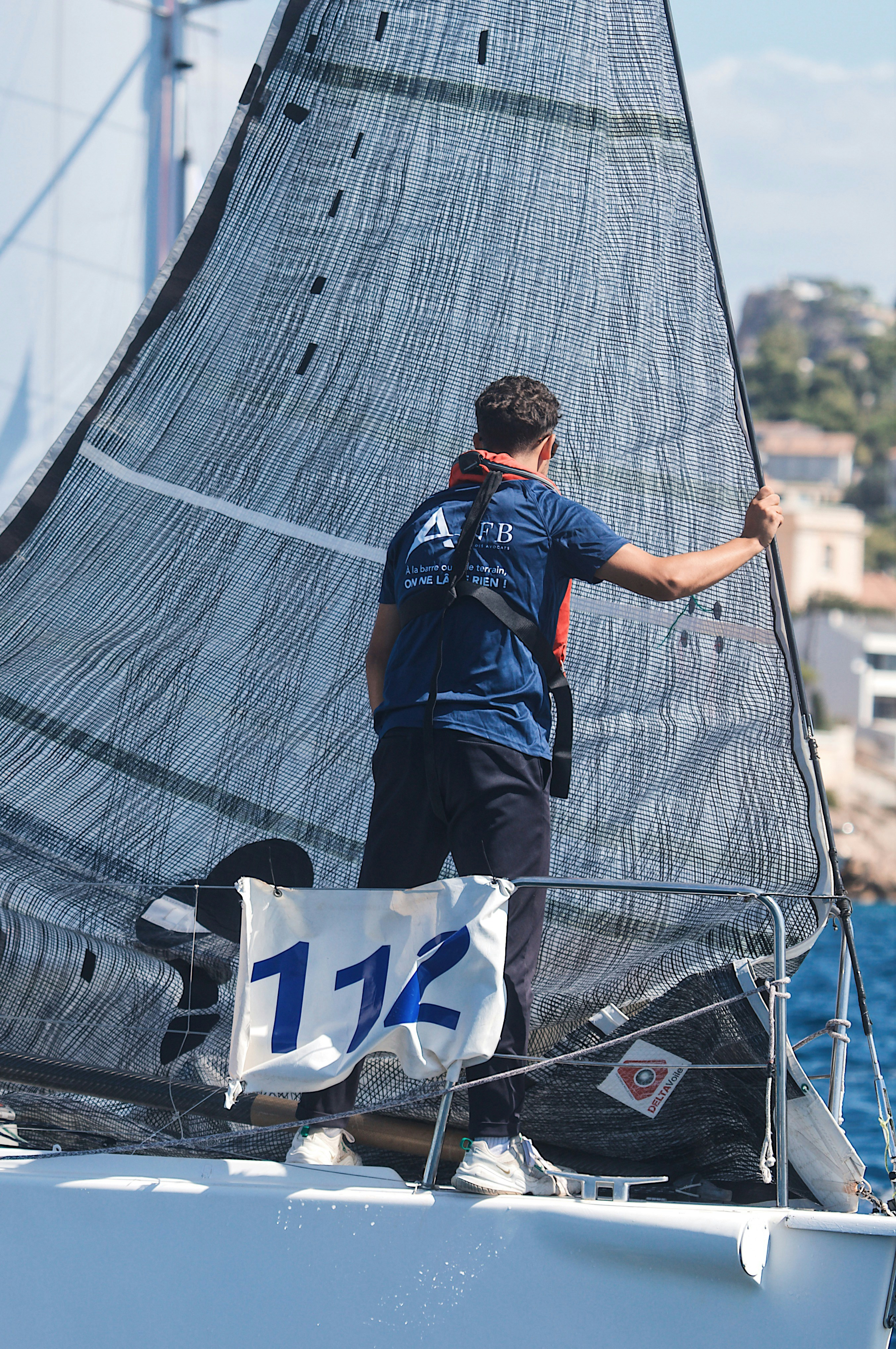 A person in a blue shirt holding the sail of a racing sailboat