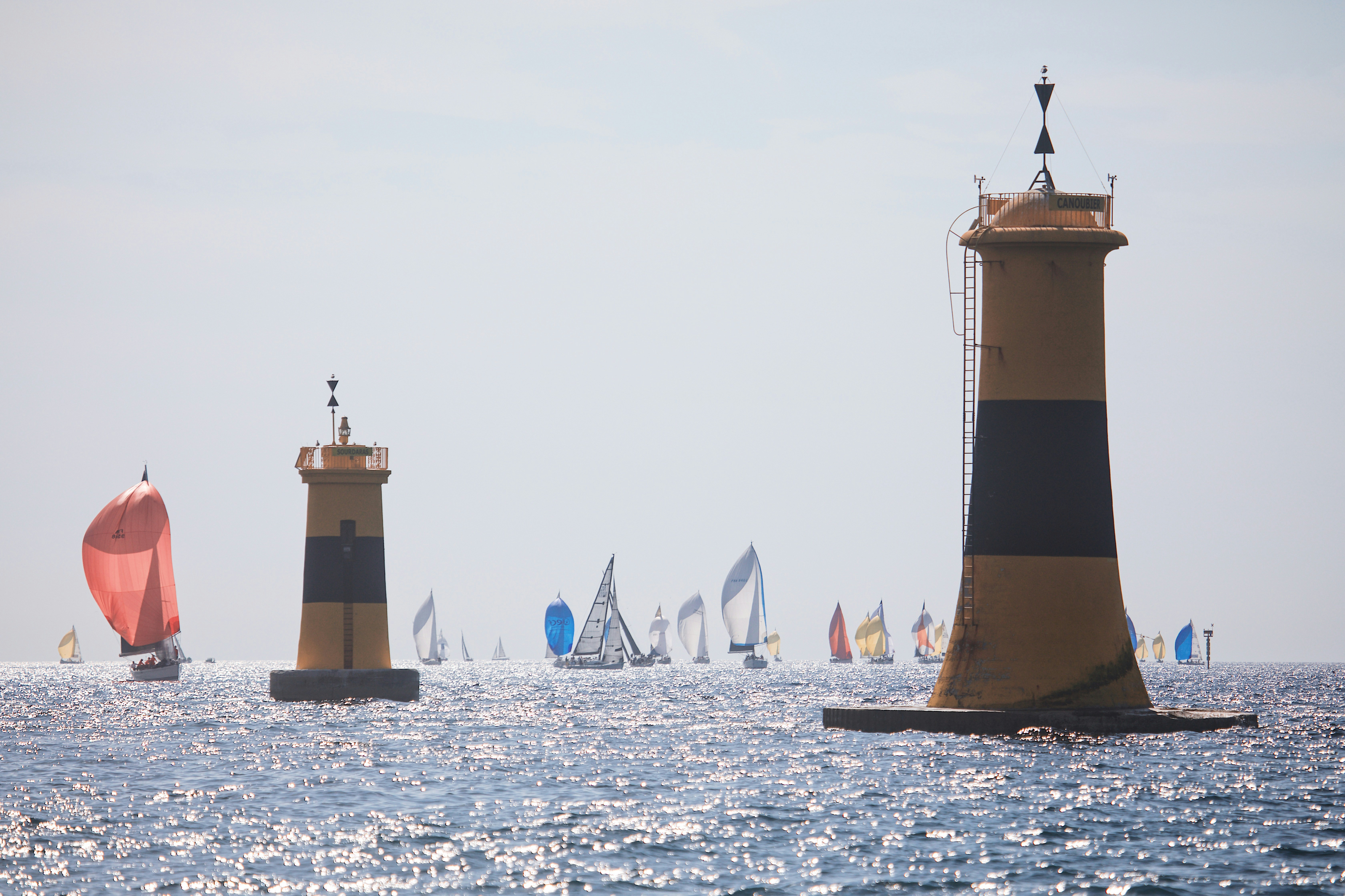 Sailboats racing past two yellow and black navigation beacons on the open sea