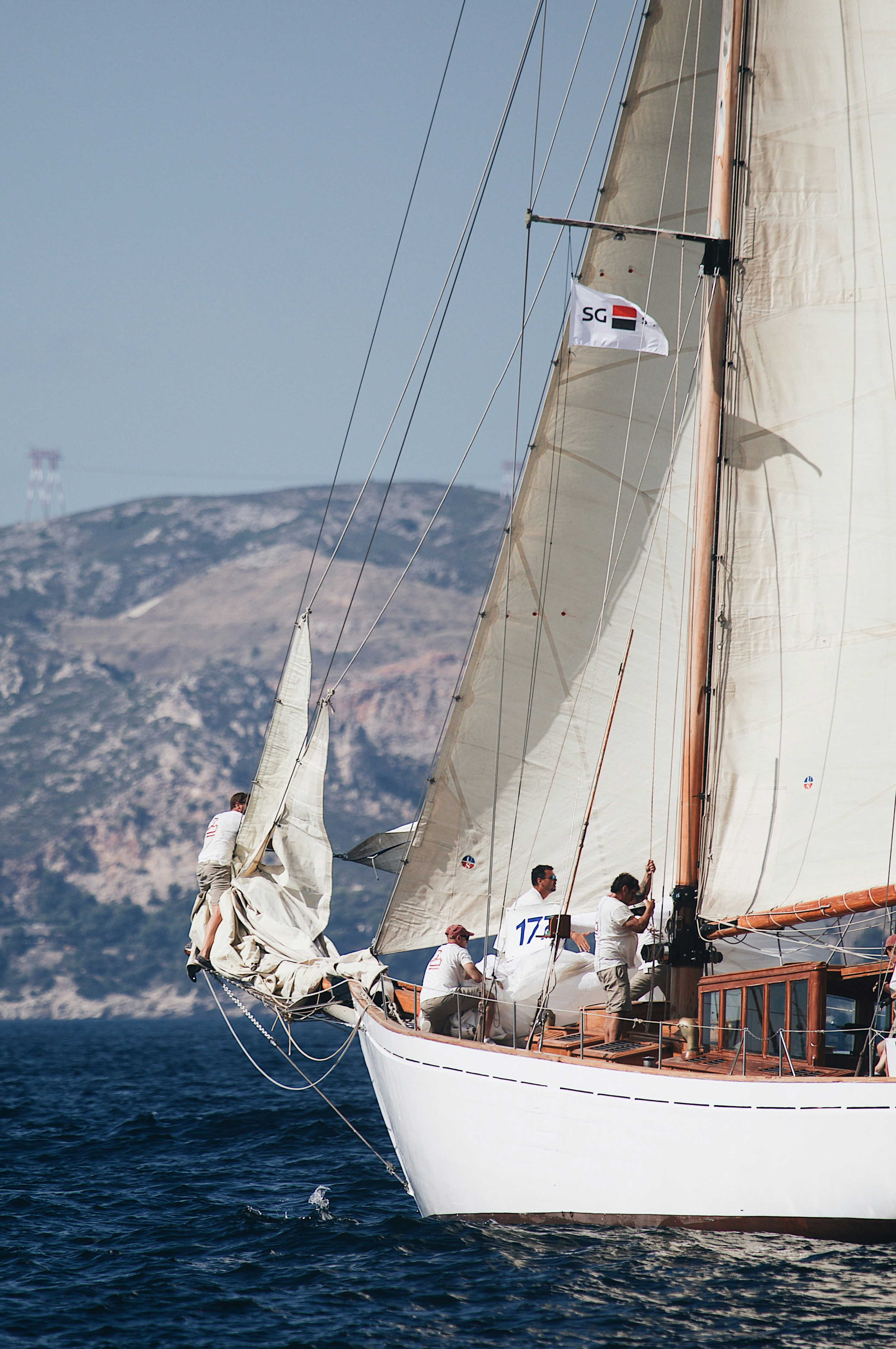 A crew of people on a wooden sailboat with white sails on the sea