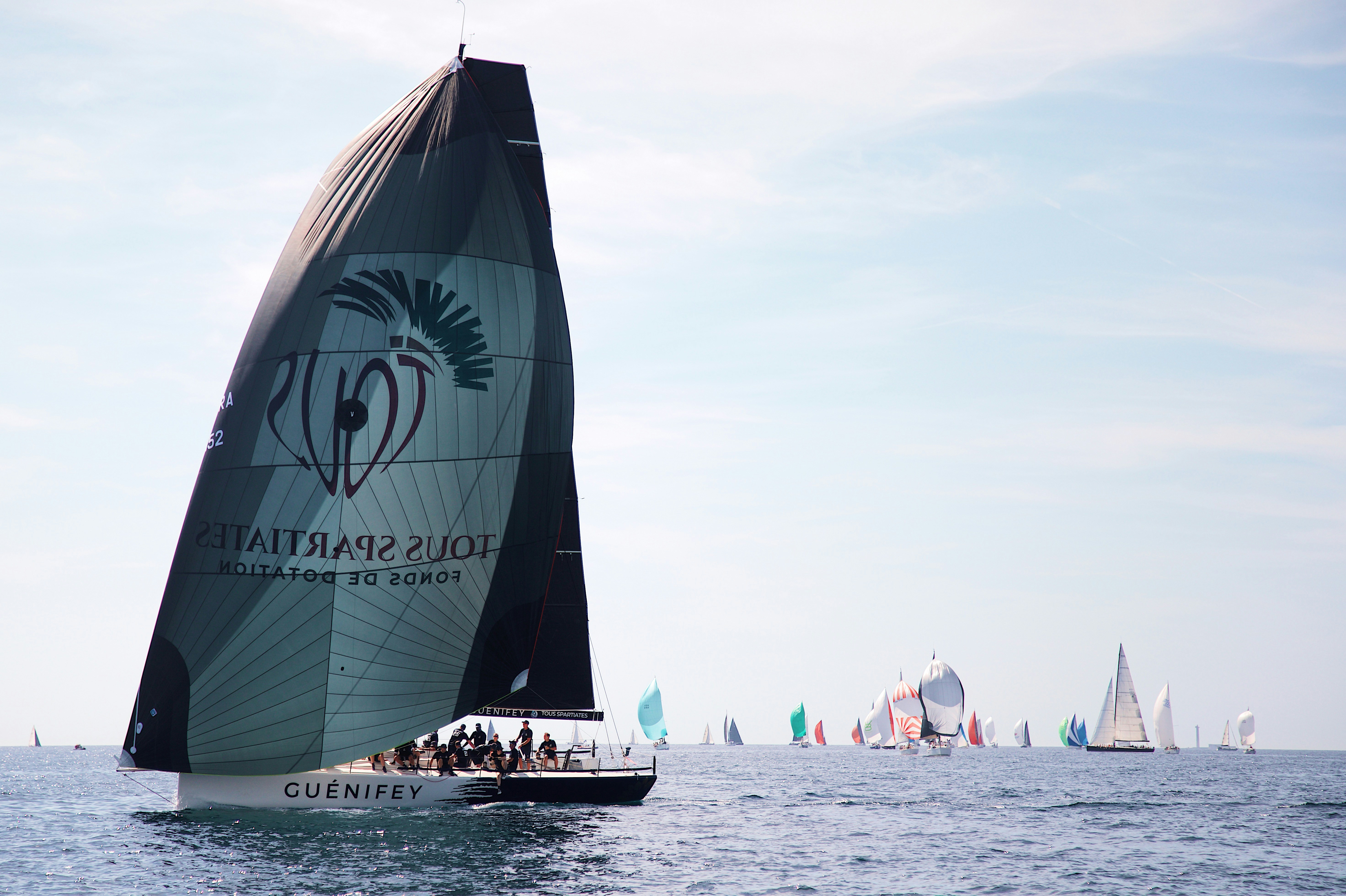 A racing sailboat with a large dark spinnaker sailing on the open sea