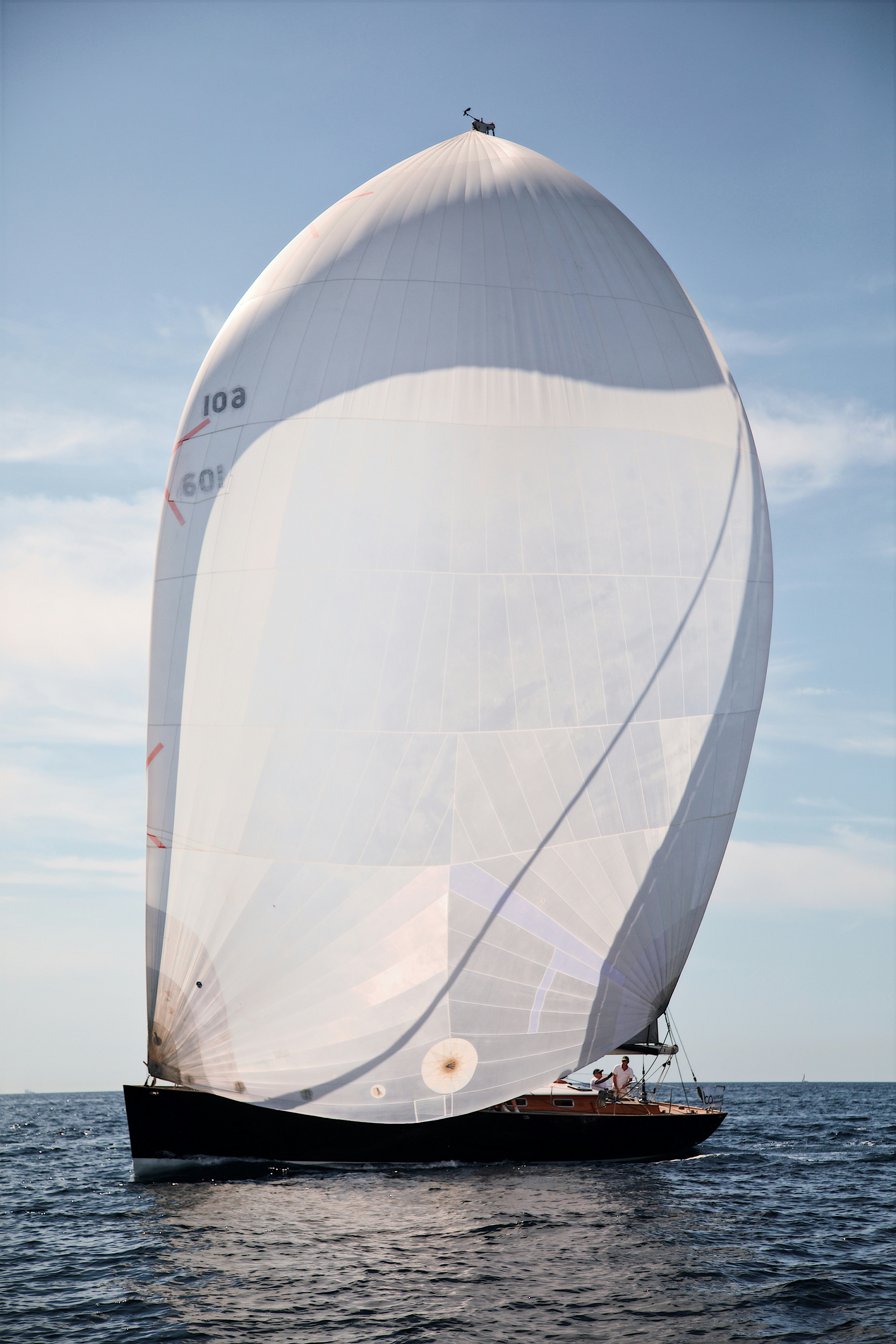 A sailboat with a large white spinnaker sail on the open blue ocean