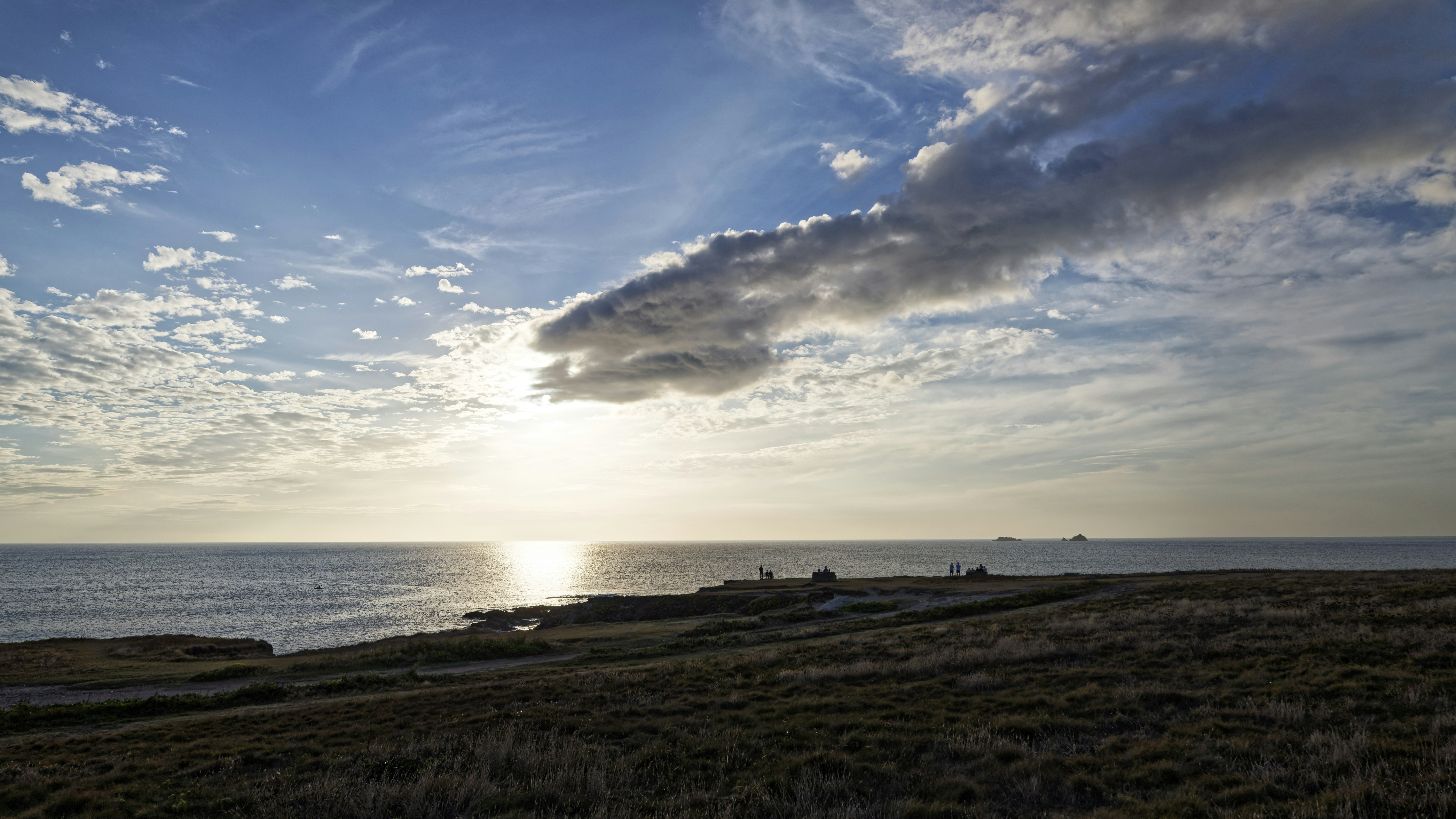 Low sun over the ocean with a rocky coastline and scattered clouds
