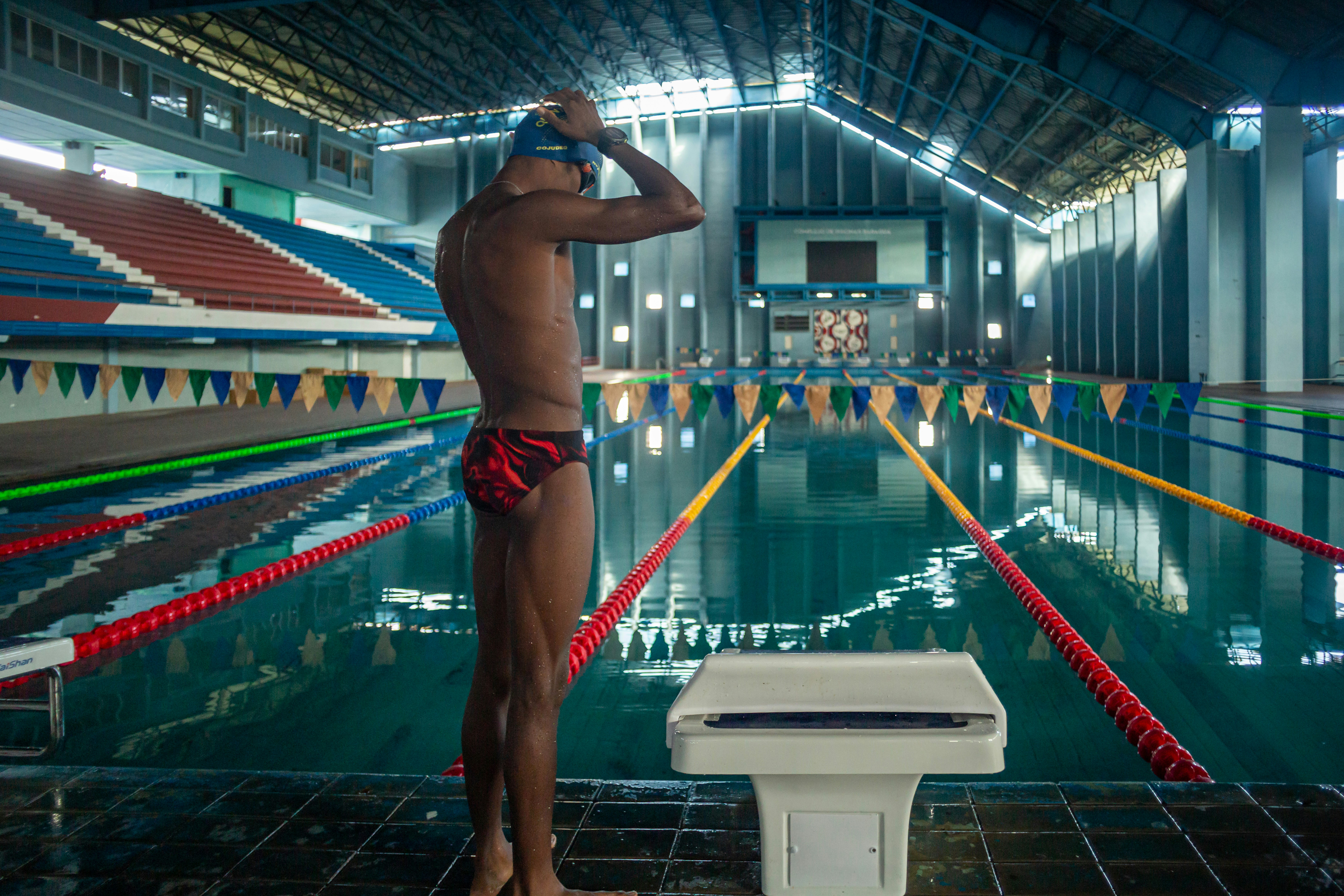 A swimmer adjusting a blue cap at the edge of an indoor pool