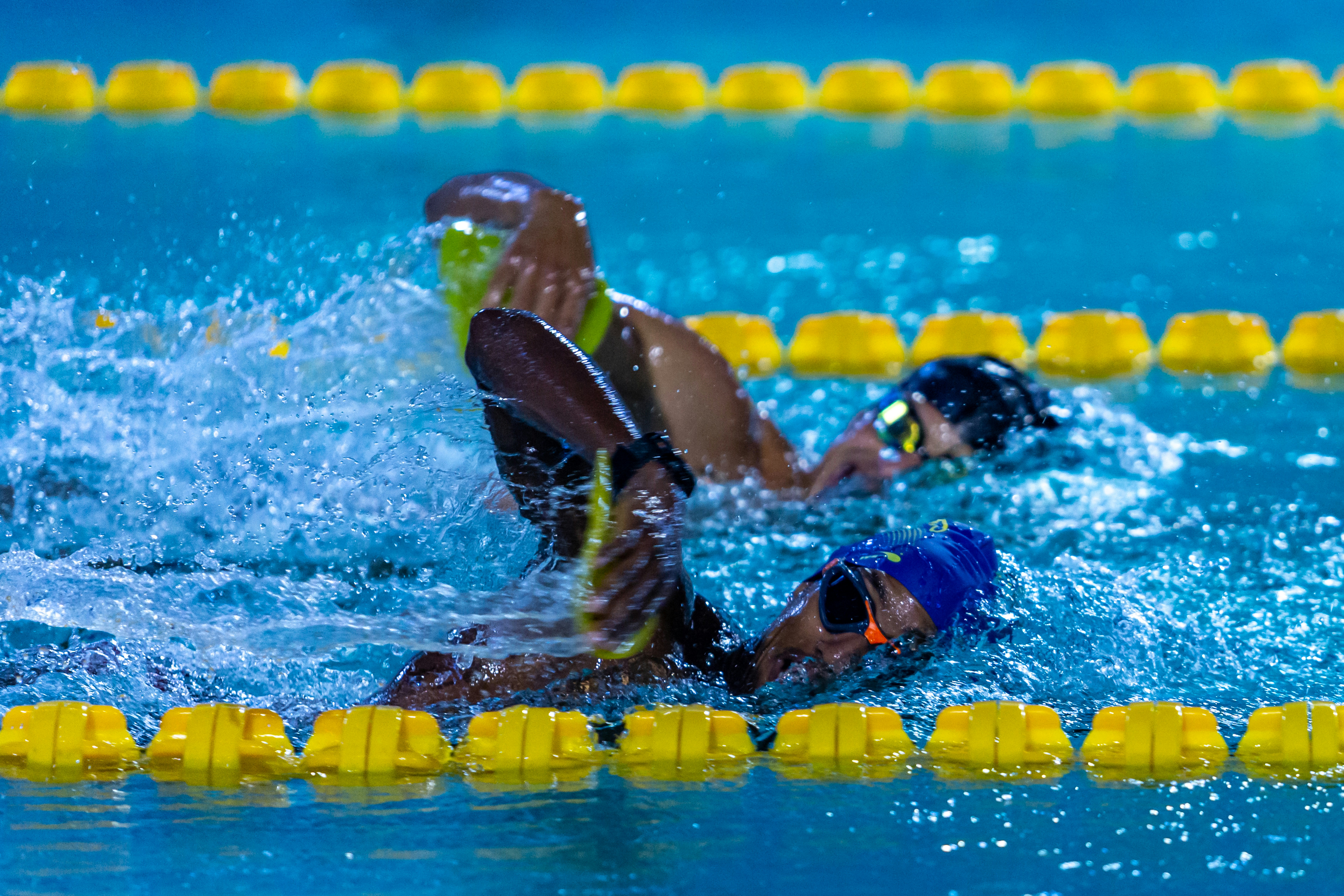 Two swimmers using yellow hand paddles in a blue pool with lane markers