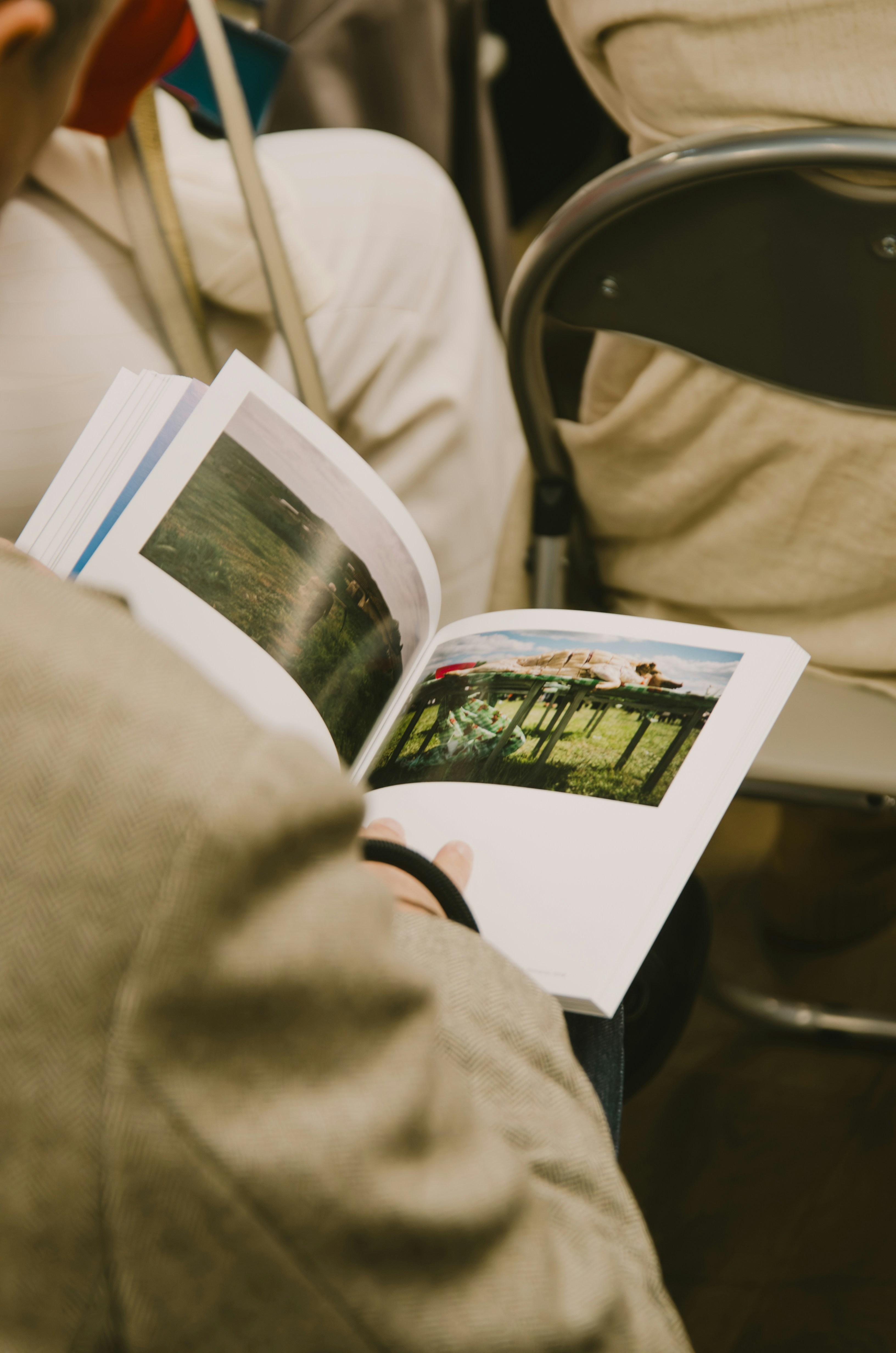 Une personne en veste beige tenant un livre ouvert avec des photos de paysages
