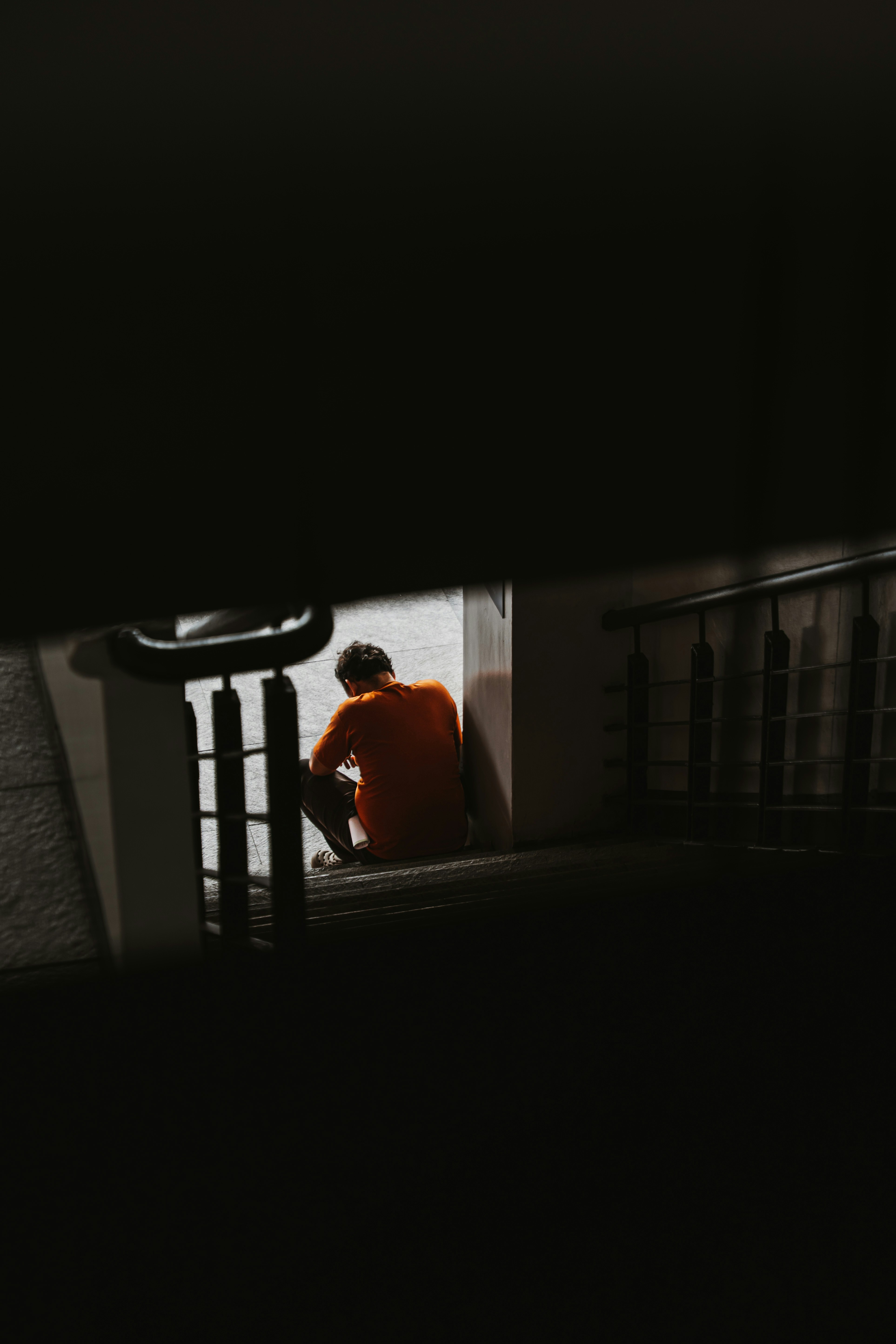 A person in an orange shirt sitting on stairs in a dimly lit hallway