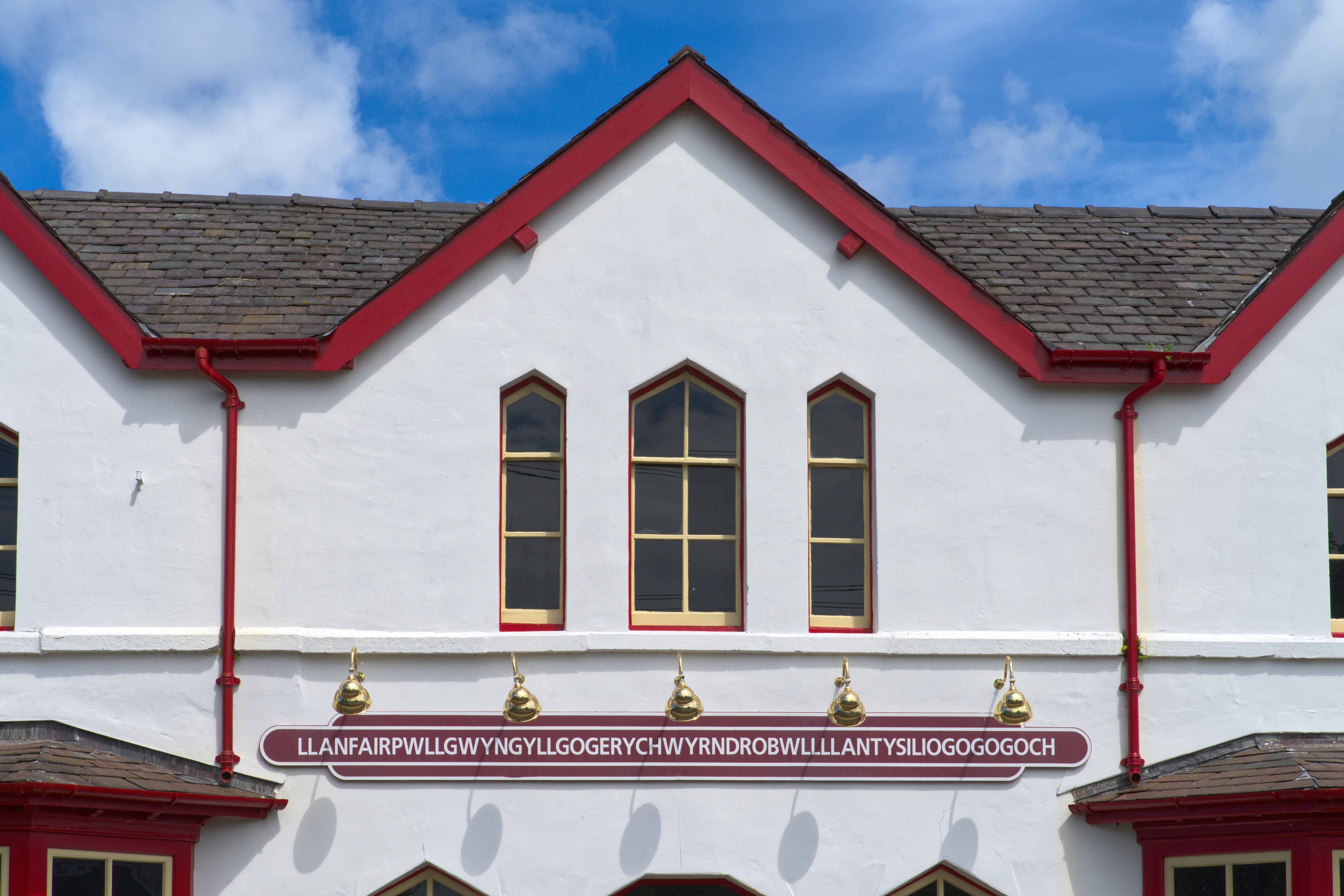 A white building with red trim and a sign reading "LLANFAIRPWLLGWYNGYLLGOGERYCHWYNDROBWLLLLANTYSILIOGOGOGOCH"