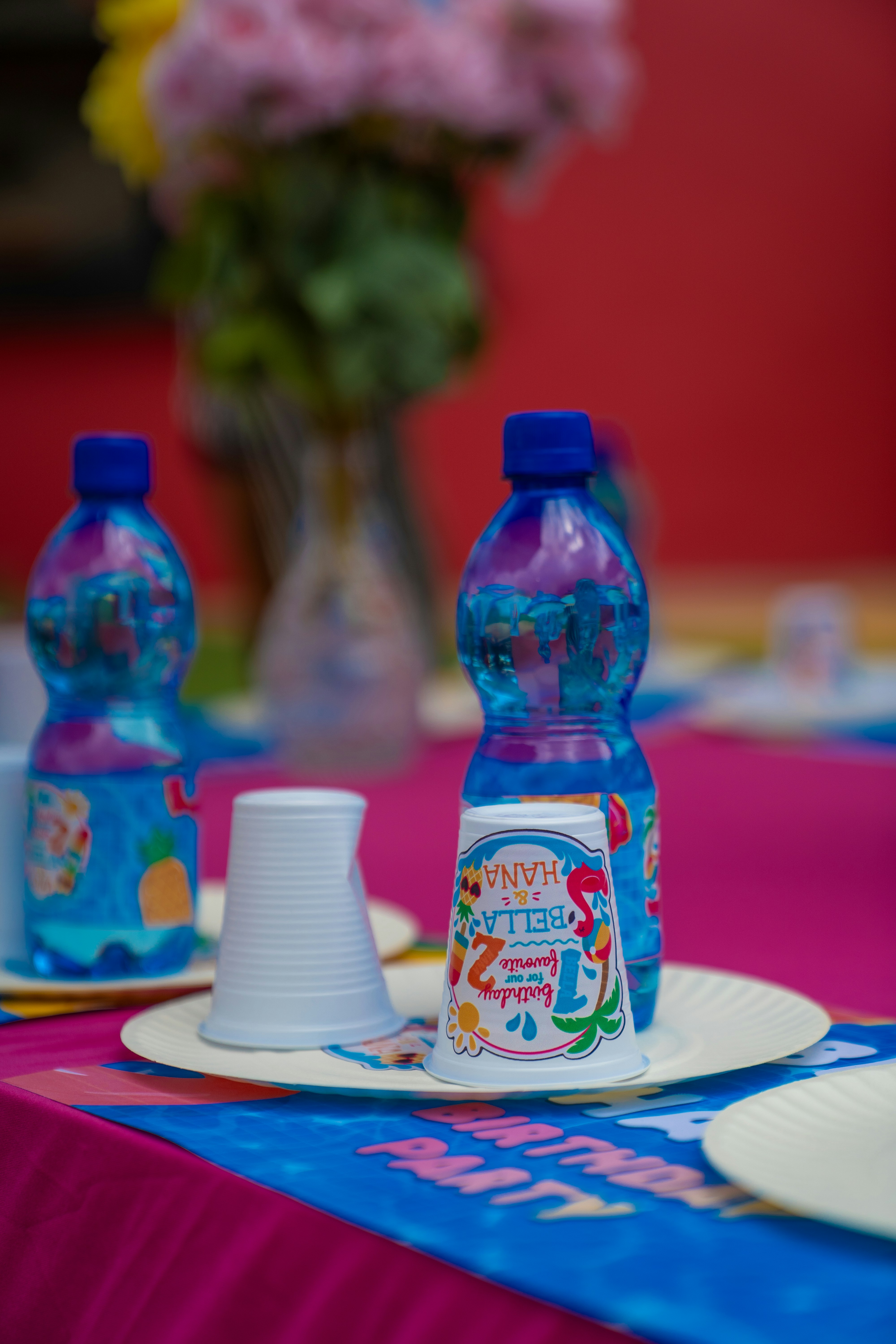 Two blue water bottles and two paper cups on a pink birthday party table