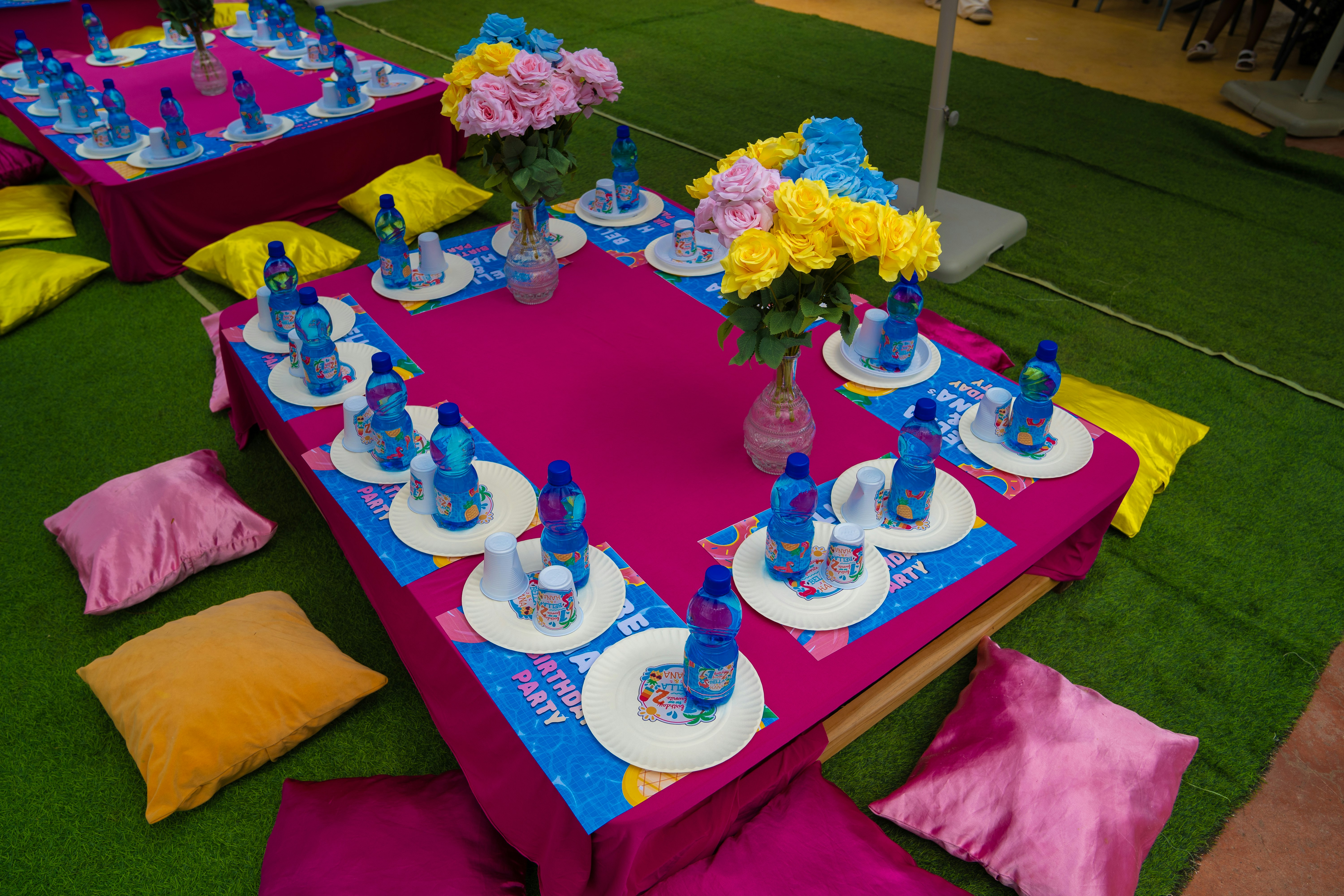 Low tables with pink cloths, floral centerpieces, and place settings on green turf
