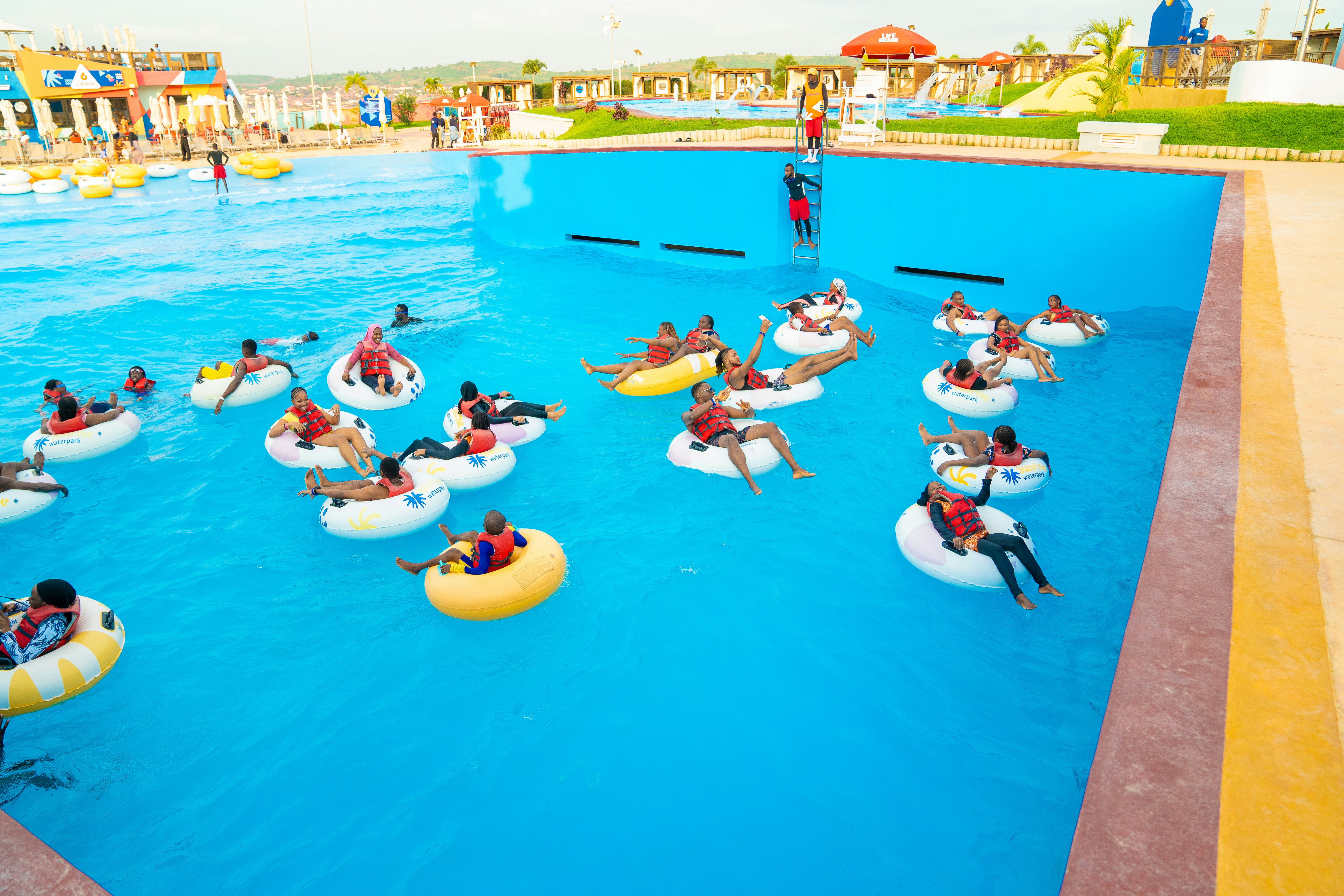 Orang-orang dengan rompi pelampung mengapung di atas ban dalam di kolam renang waterpark biru yang besar