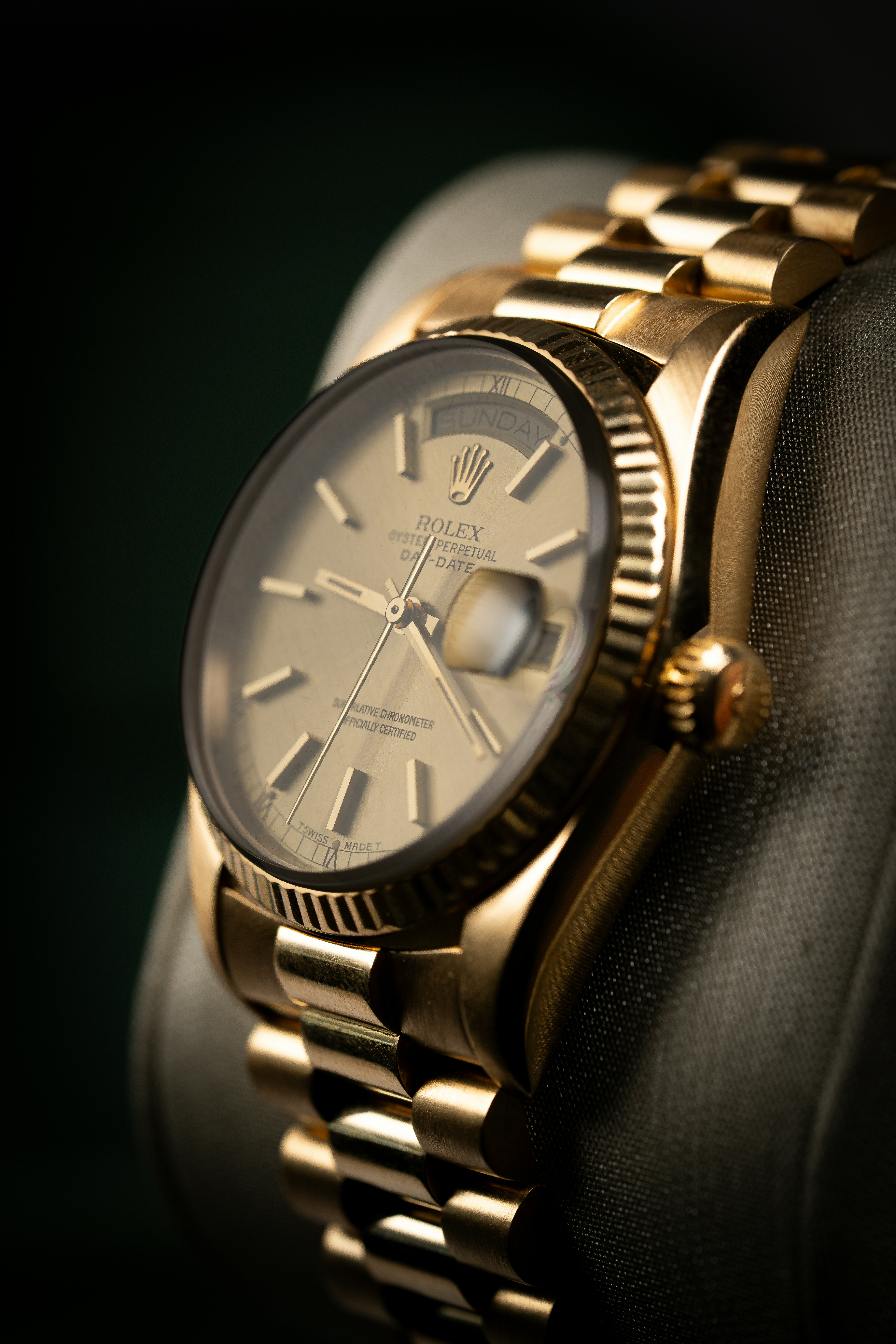 A gold wristwatch with a fluted bezel and metallic dial on a display cushion