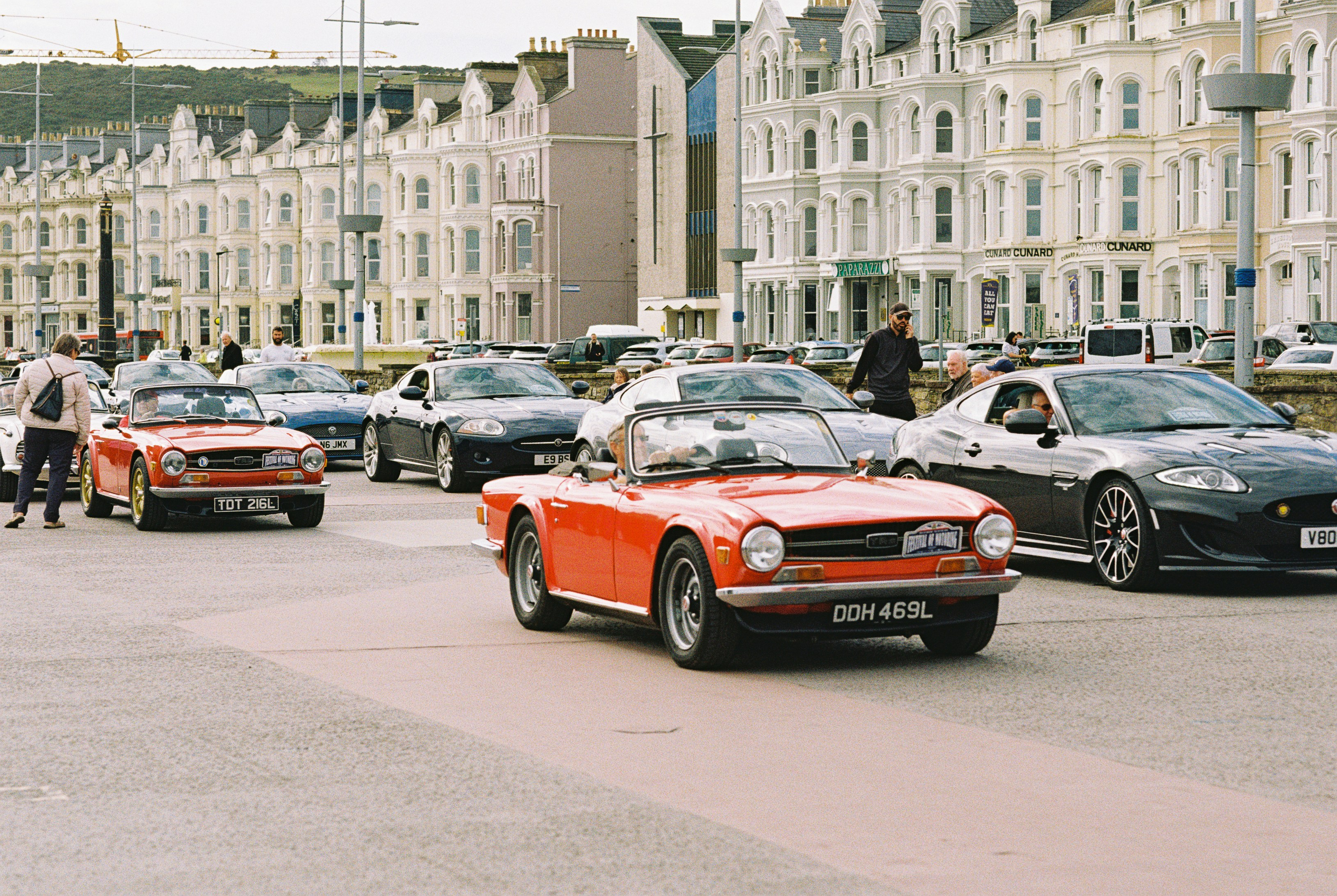 A group of vintage and modern cars driving along a coastal promenade