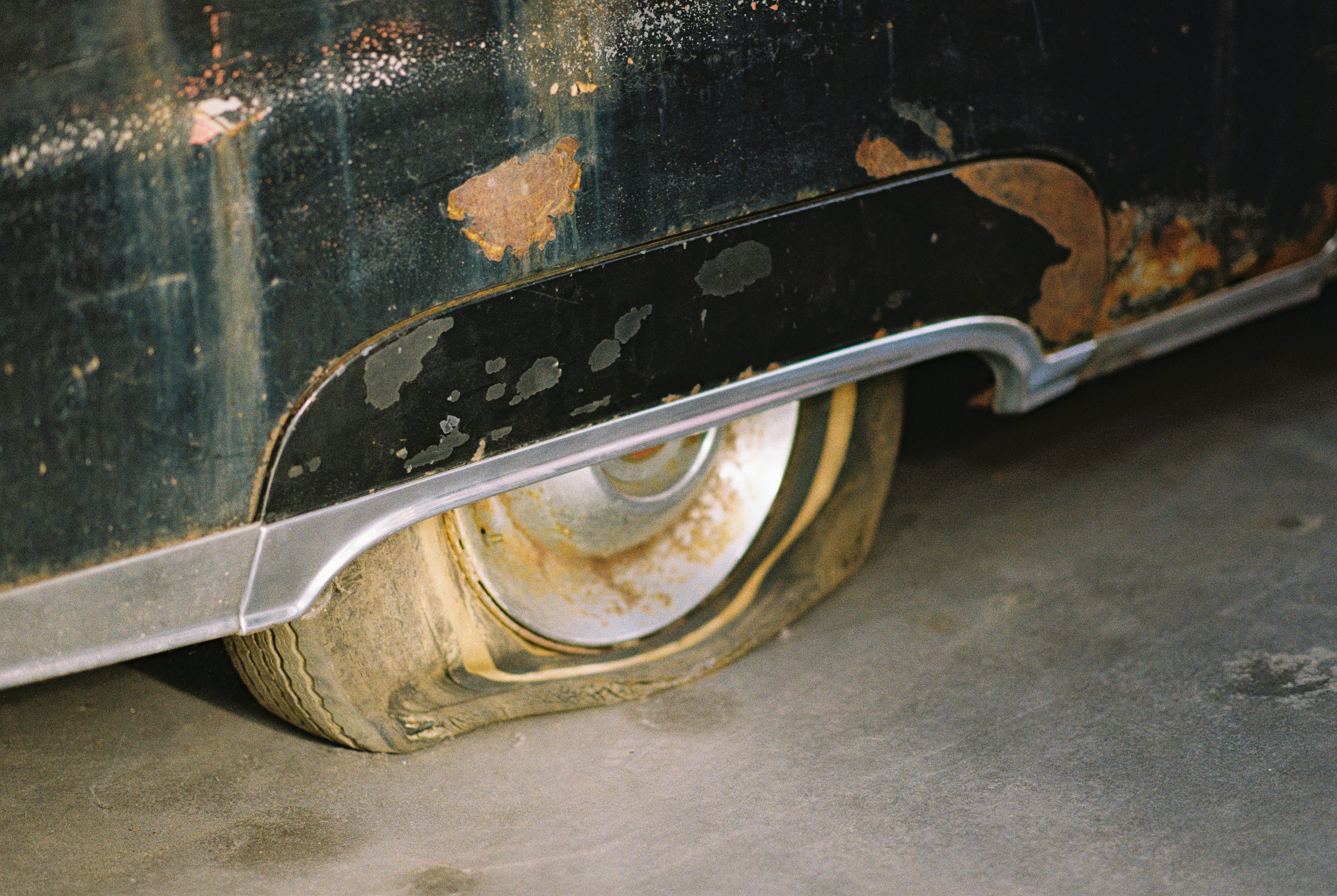 A flat tire on a rusted black vintage car on a concrete floor