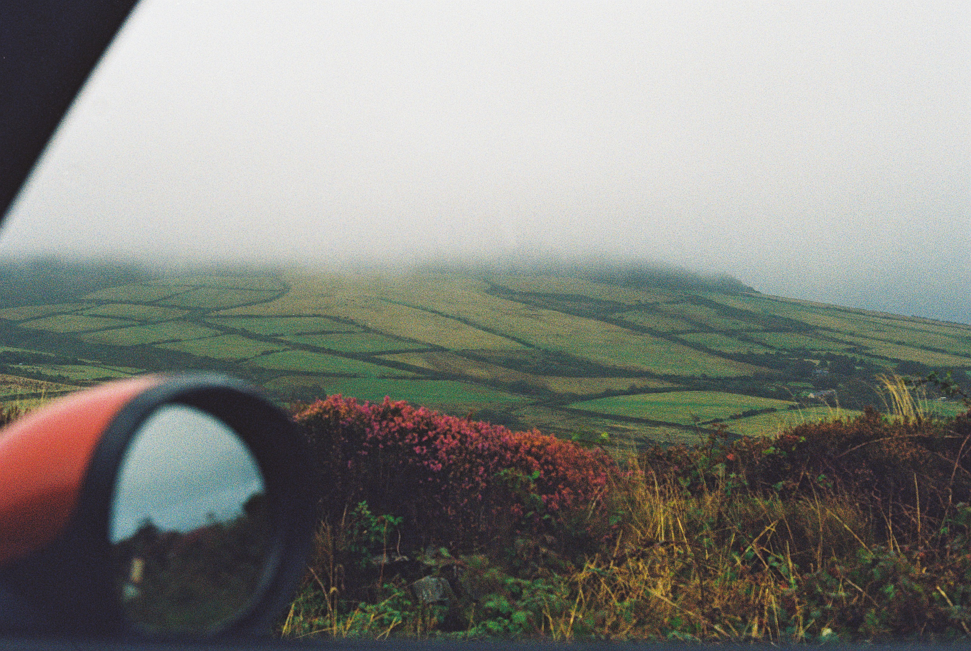 A view of green fields and misty hills from a car side mirror