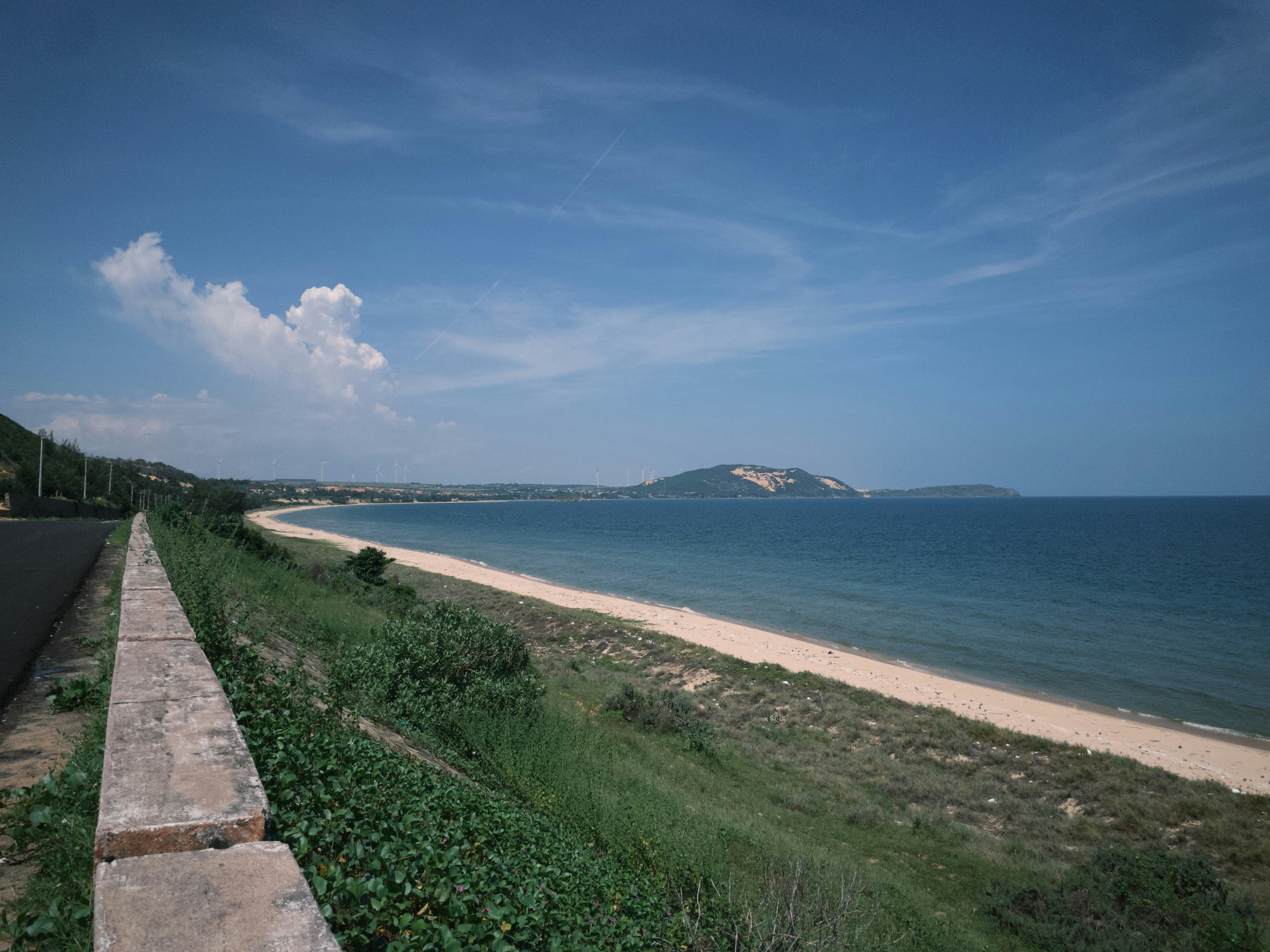 A coastal road beside a sandy beach and blue ocean under a clear sky