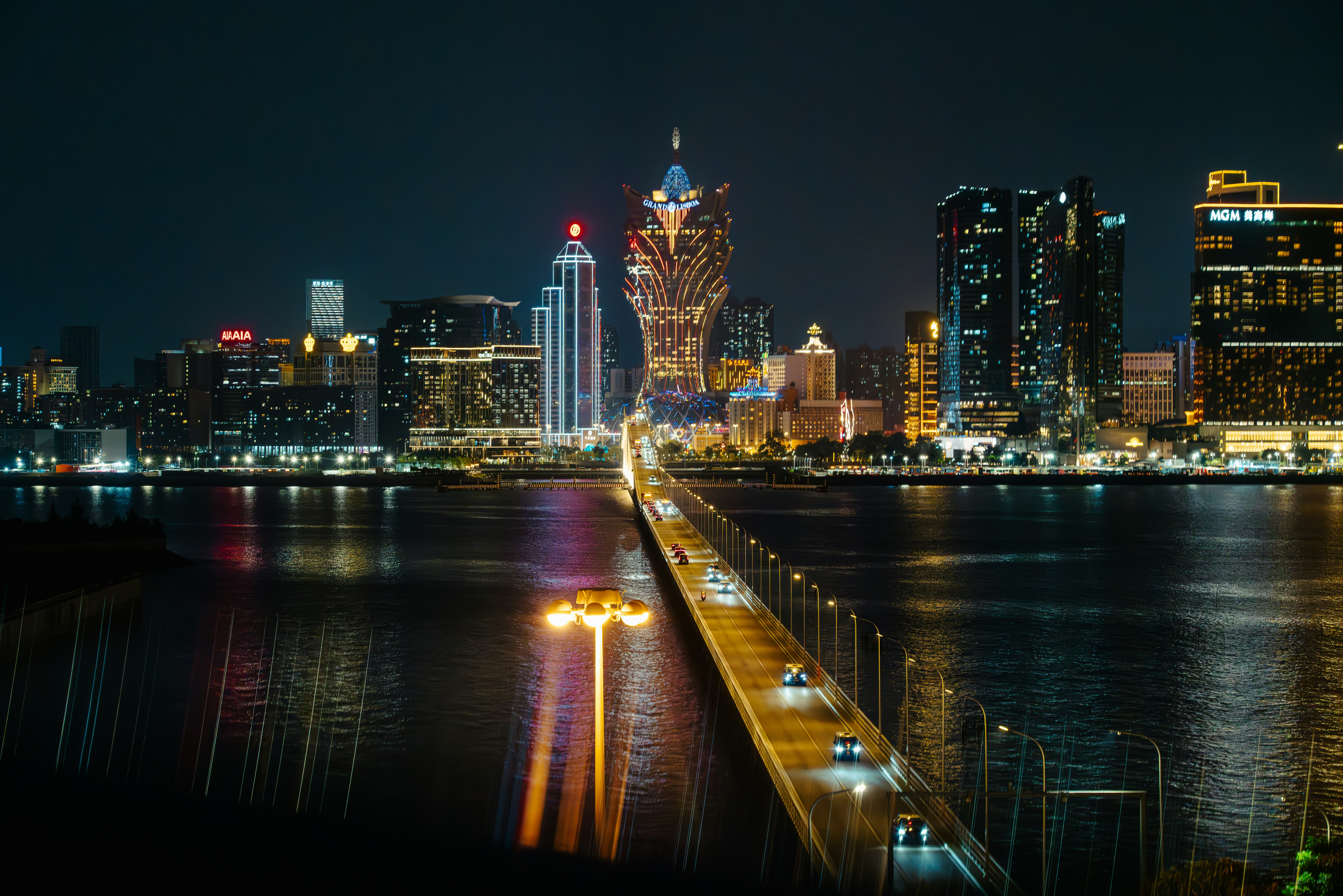 A long bridge with traffic leading to the illuminated skyline of Macau at night