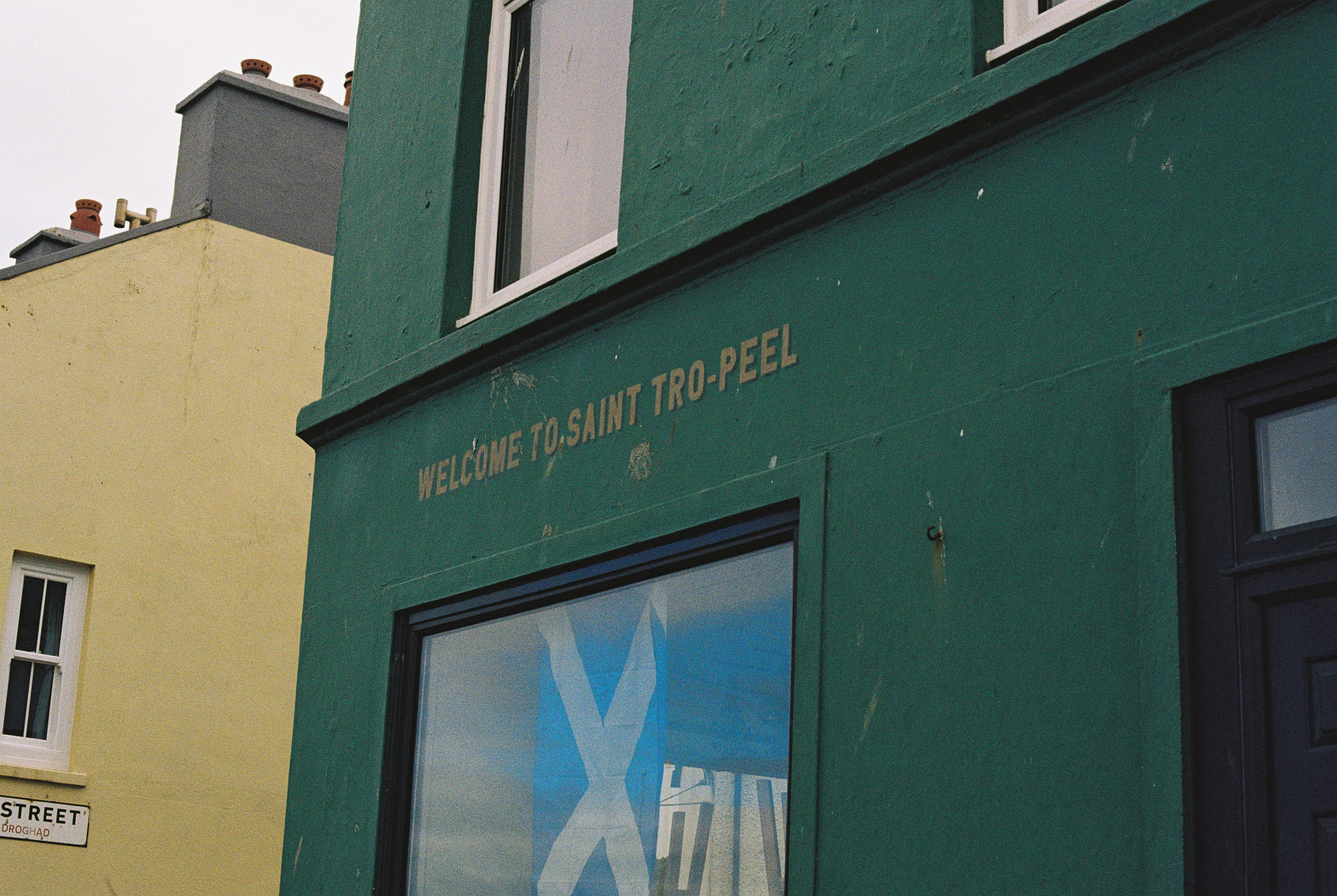 A green building with text reading WELCOME TO SAINT TRO-PEEL above a window