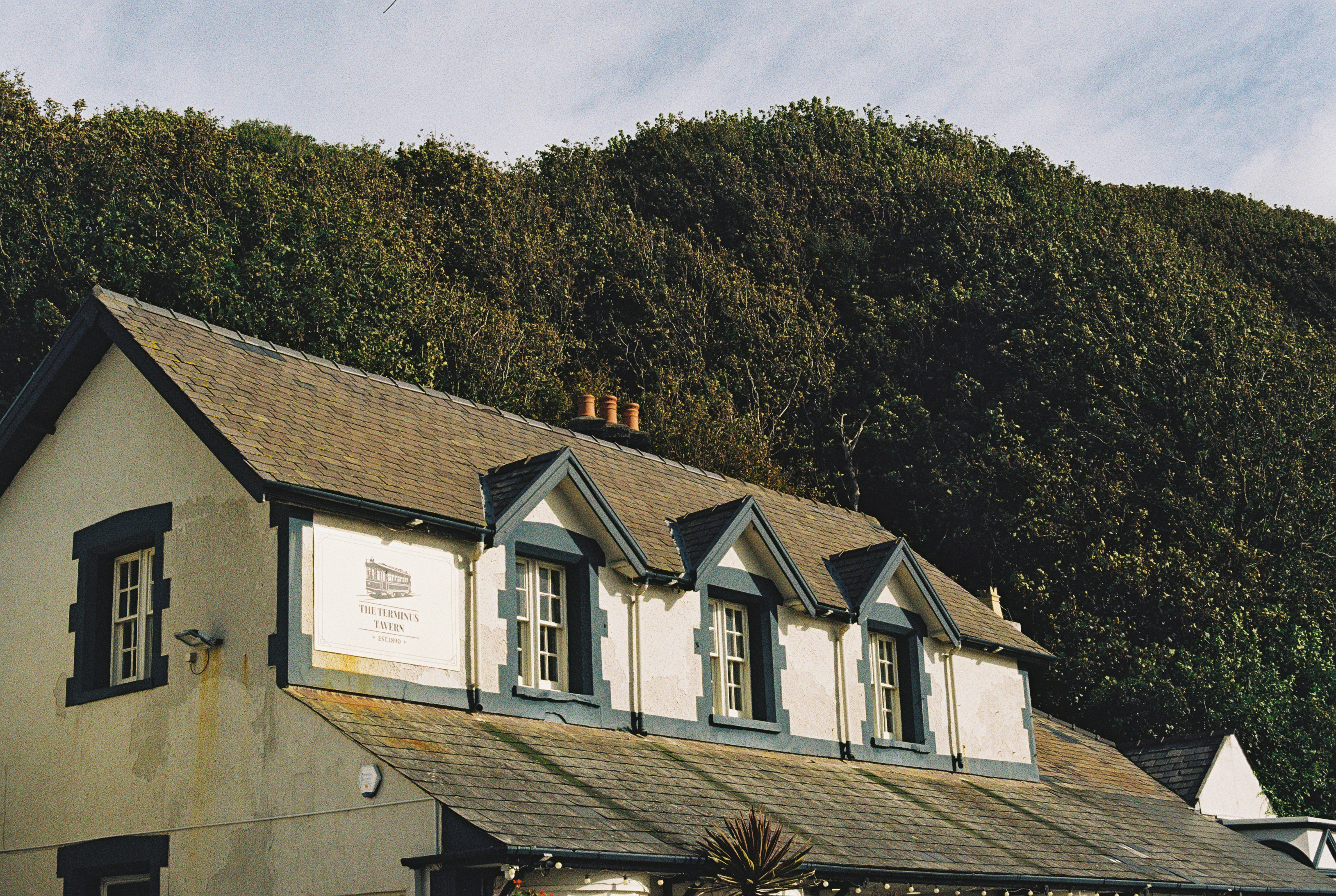 The Terminus Tavern building with a slate roof against a dense wooded hillside