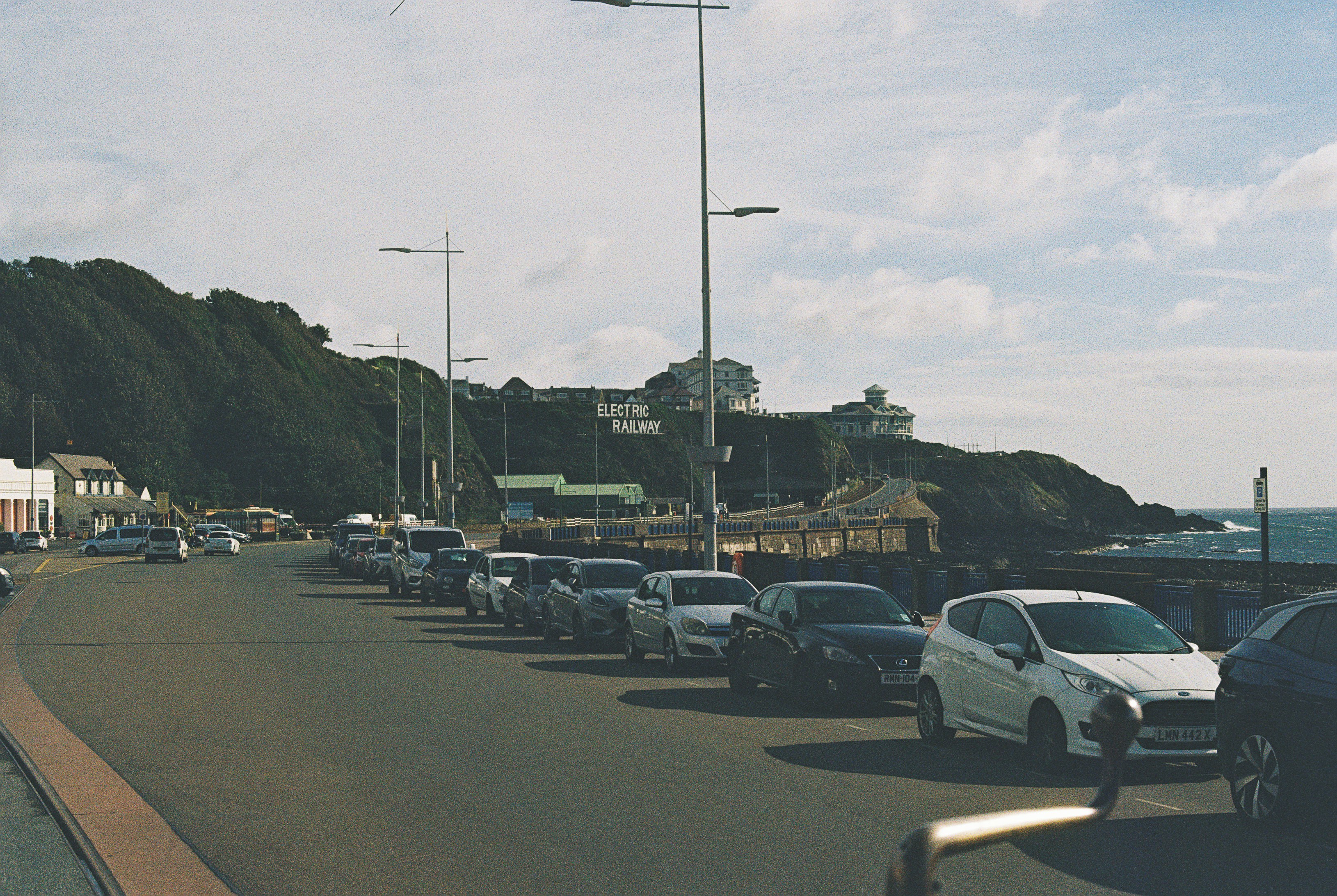 Cars parked along a coastal road with a sign reading Electric Railway