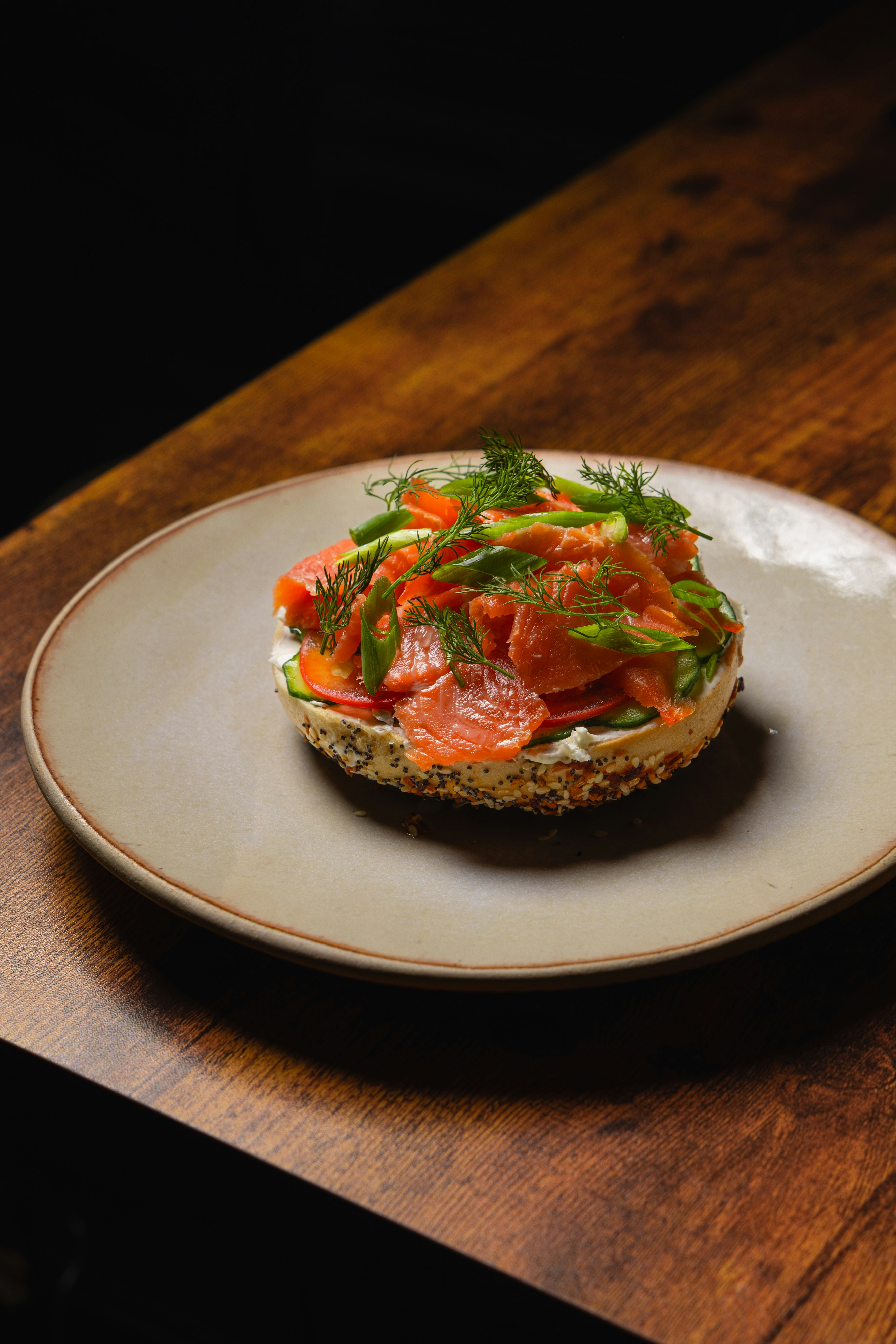 An everything bagel with cream cheese, smoked salmon, cucumber, and dill on a plate