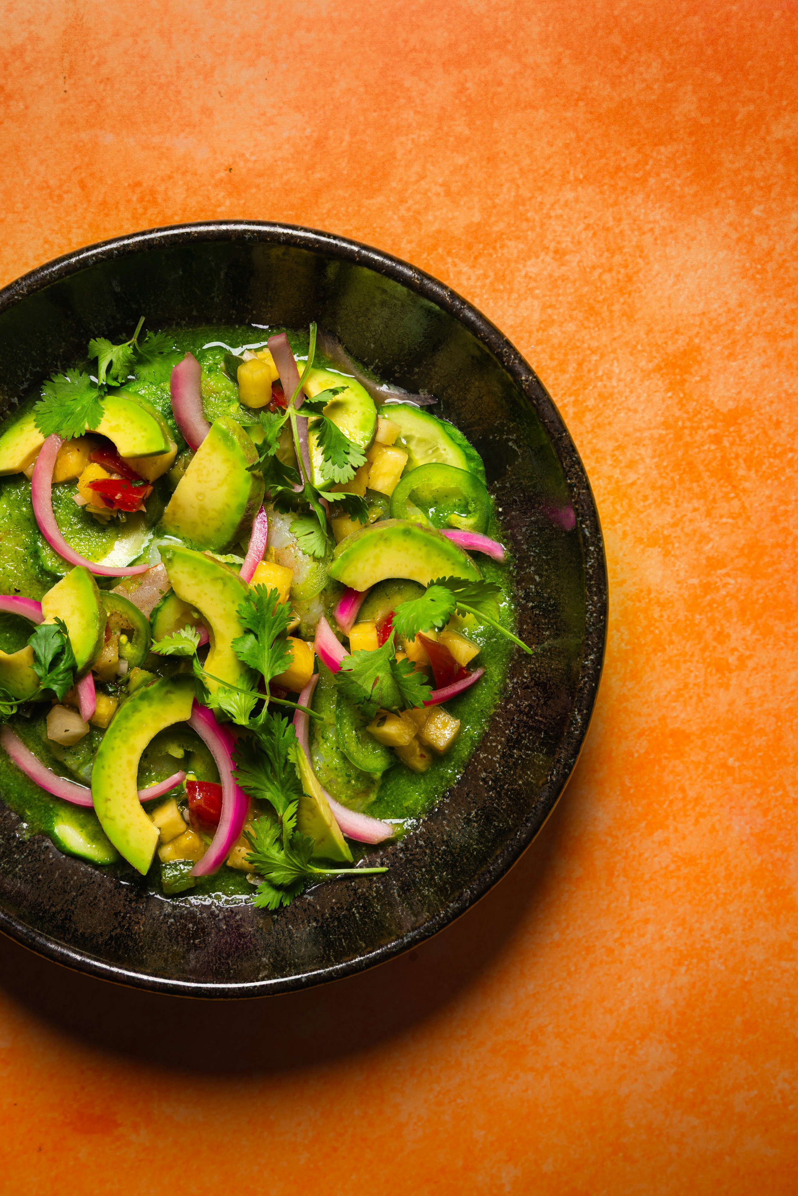 A bowl of green ceviche with avocado, red onion, and cilantro on orange