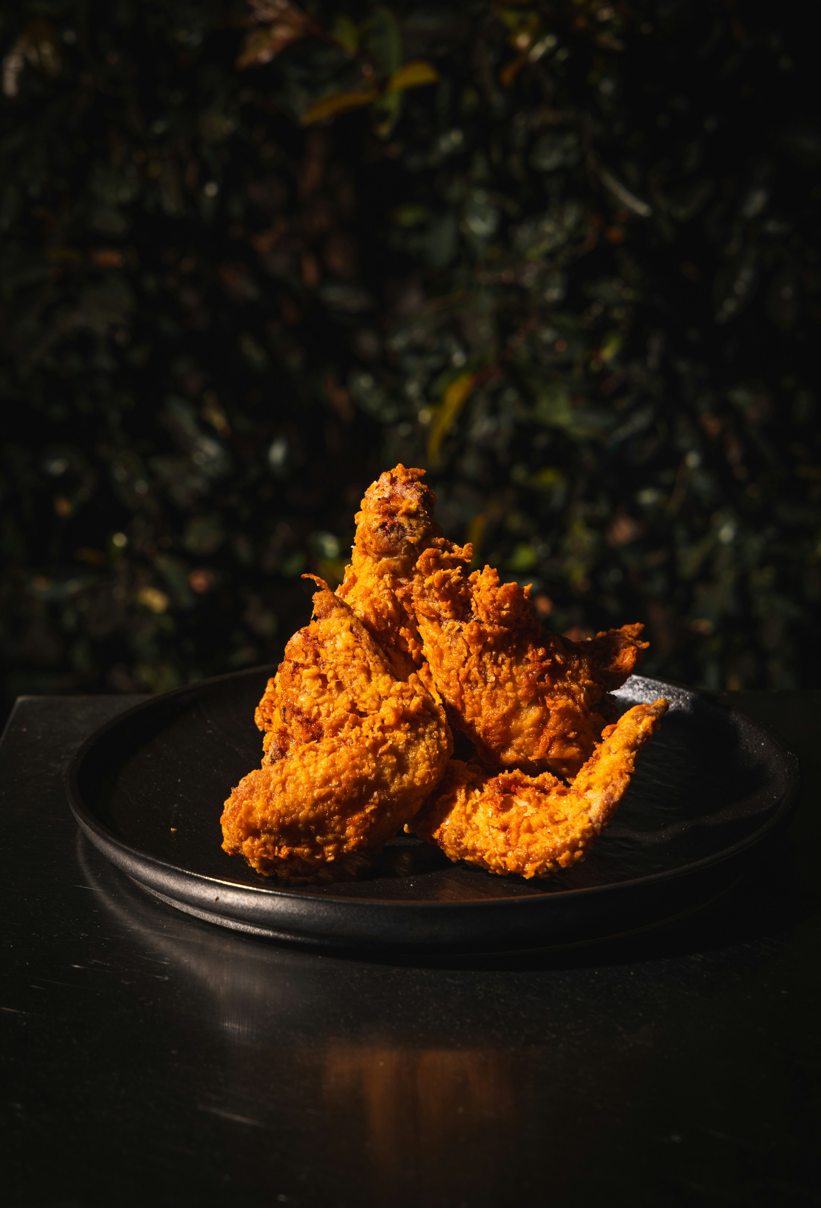 Crispy fried chicken wings on a black plate against a dark leafy background