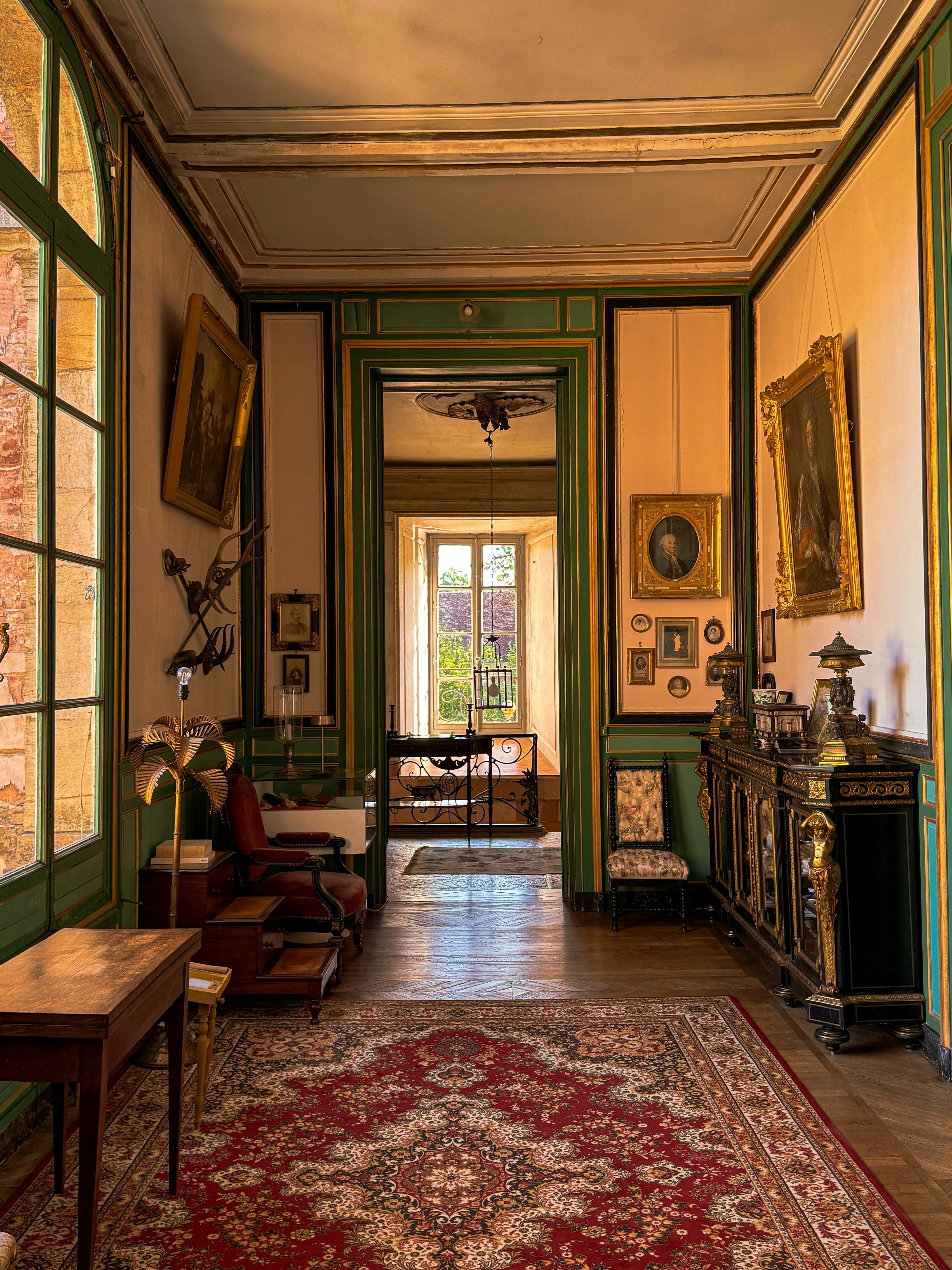 An ornate room with green trim, framed paintings, and a red patterned rug