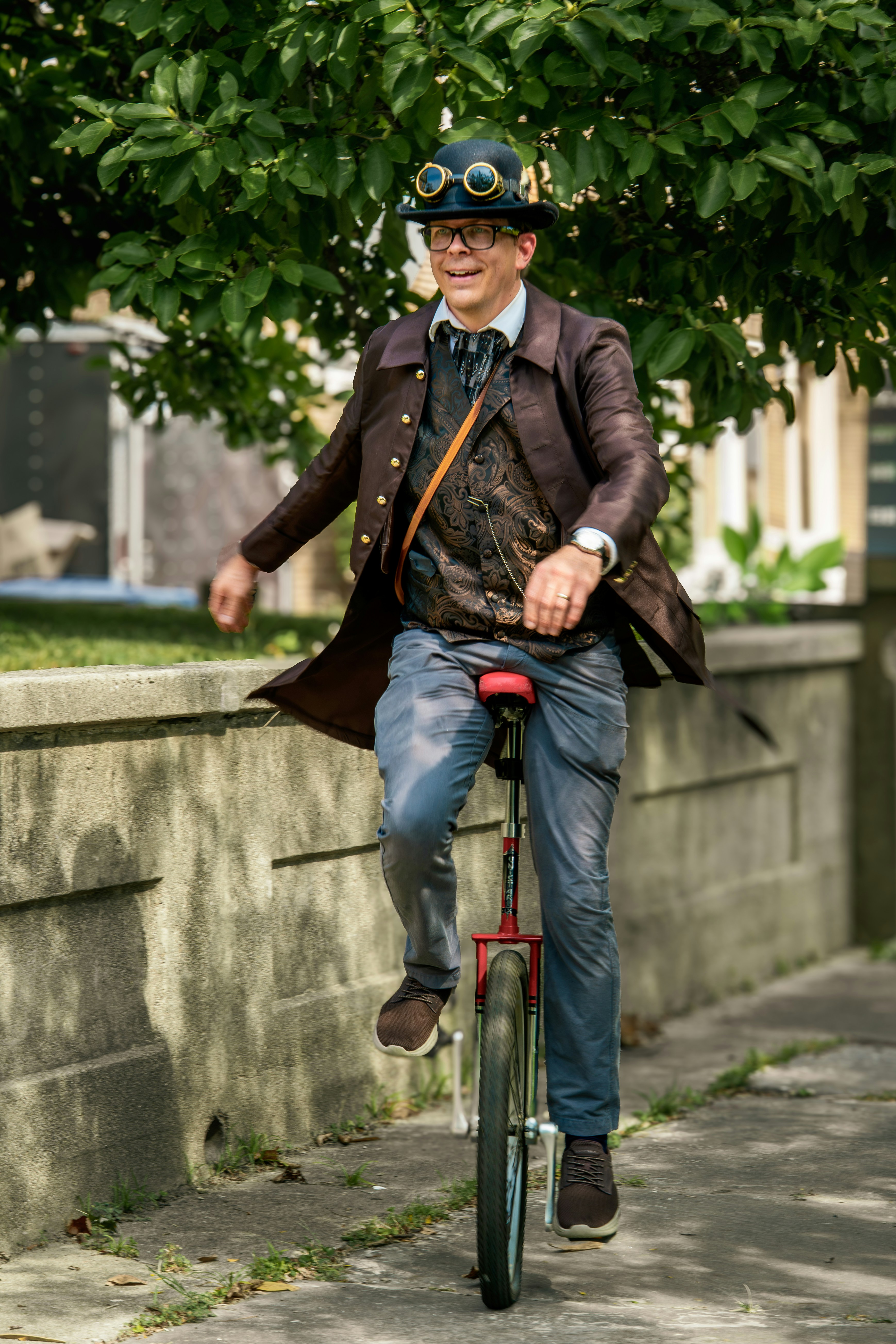A man in steampunk attire riding a unicycle along a concrete sidewalk