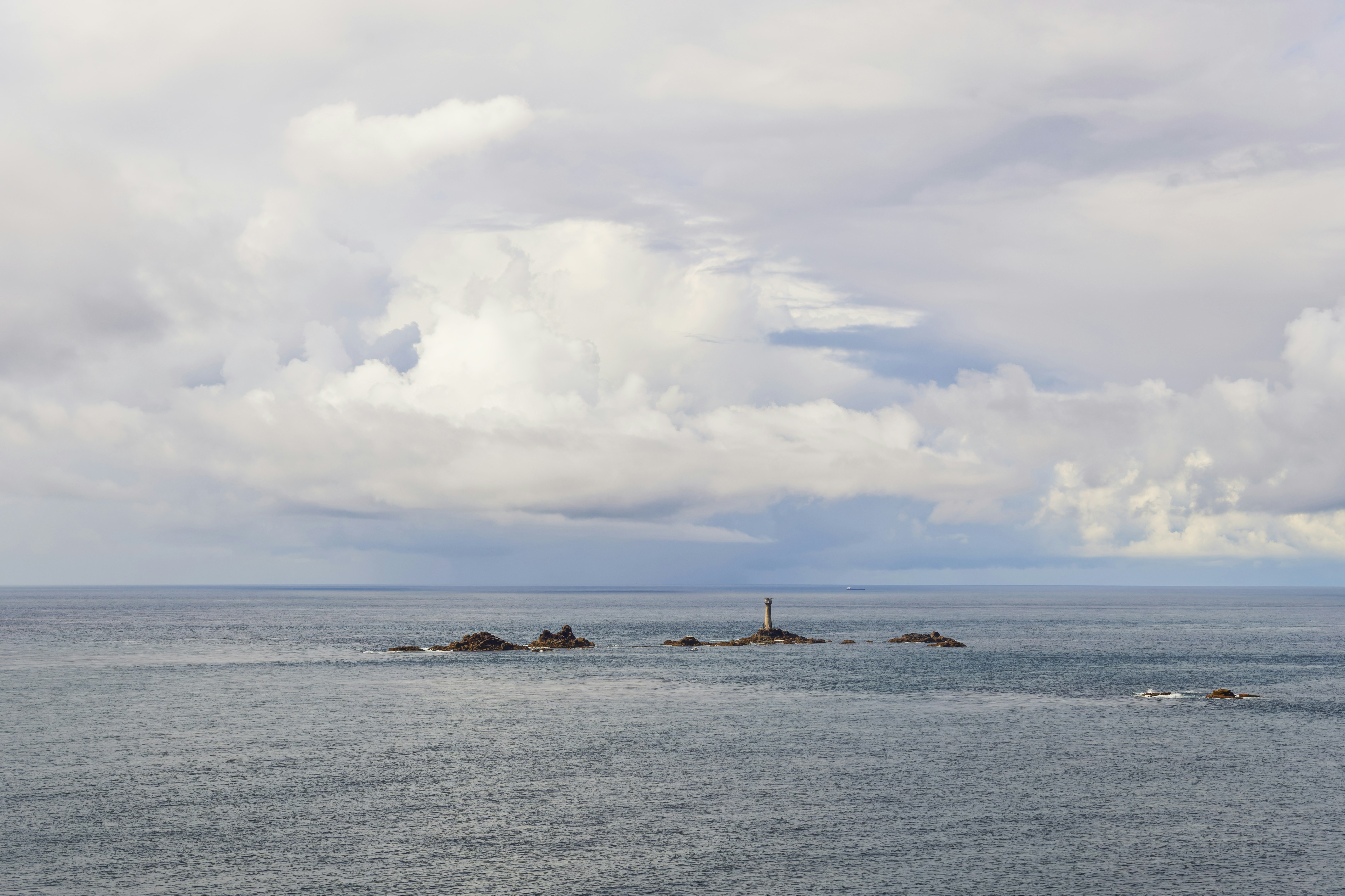 A lighthouse on a rocky outcrop in the ocean under a cloudy sky