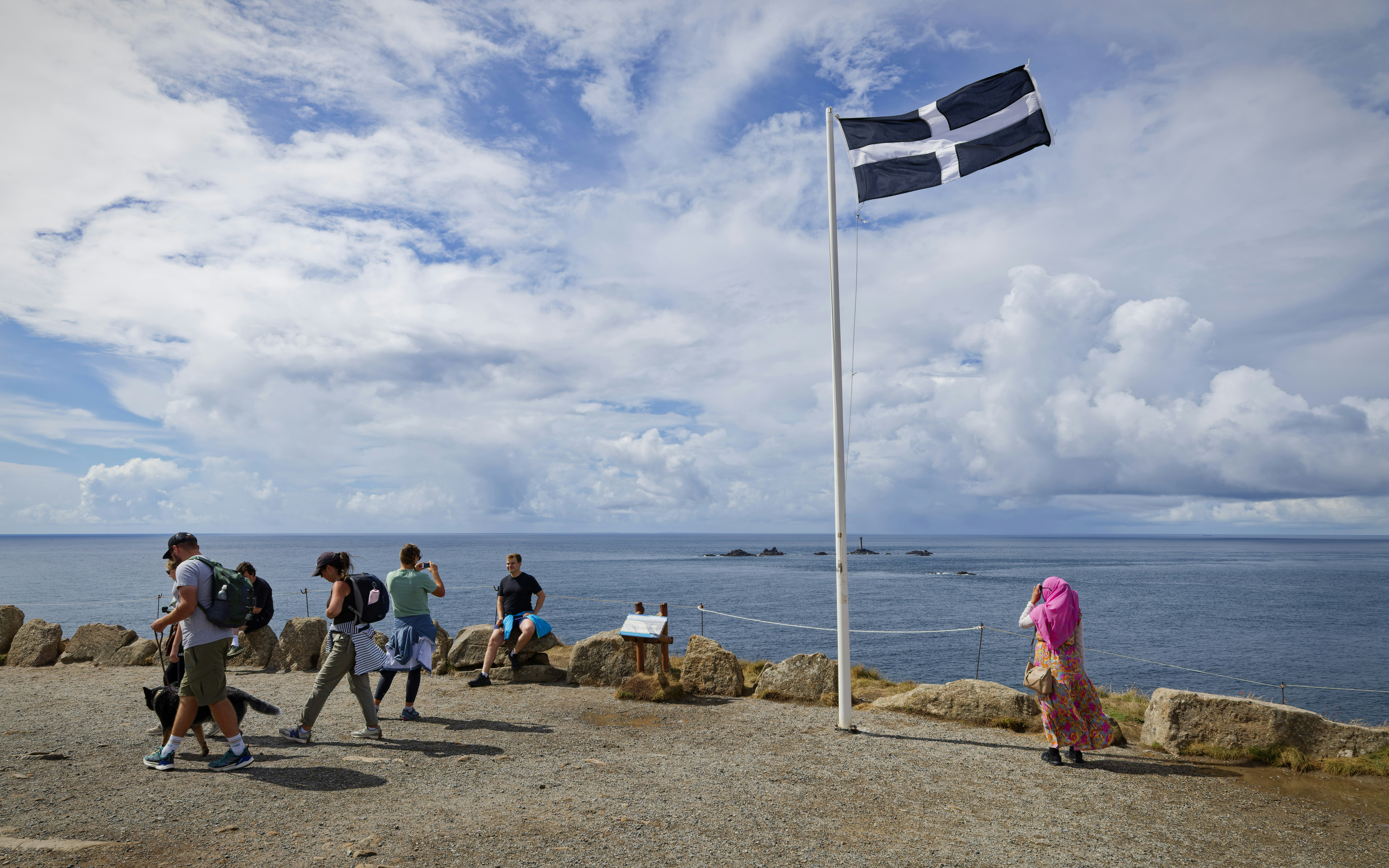 People on a rocky cliff overlooking the sea with a Saint Piran flag