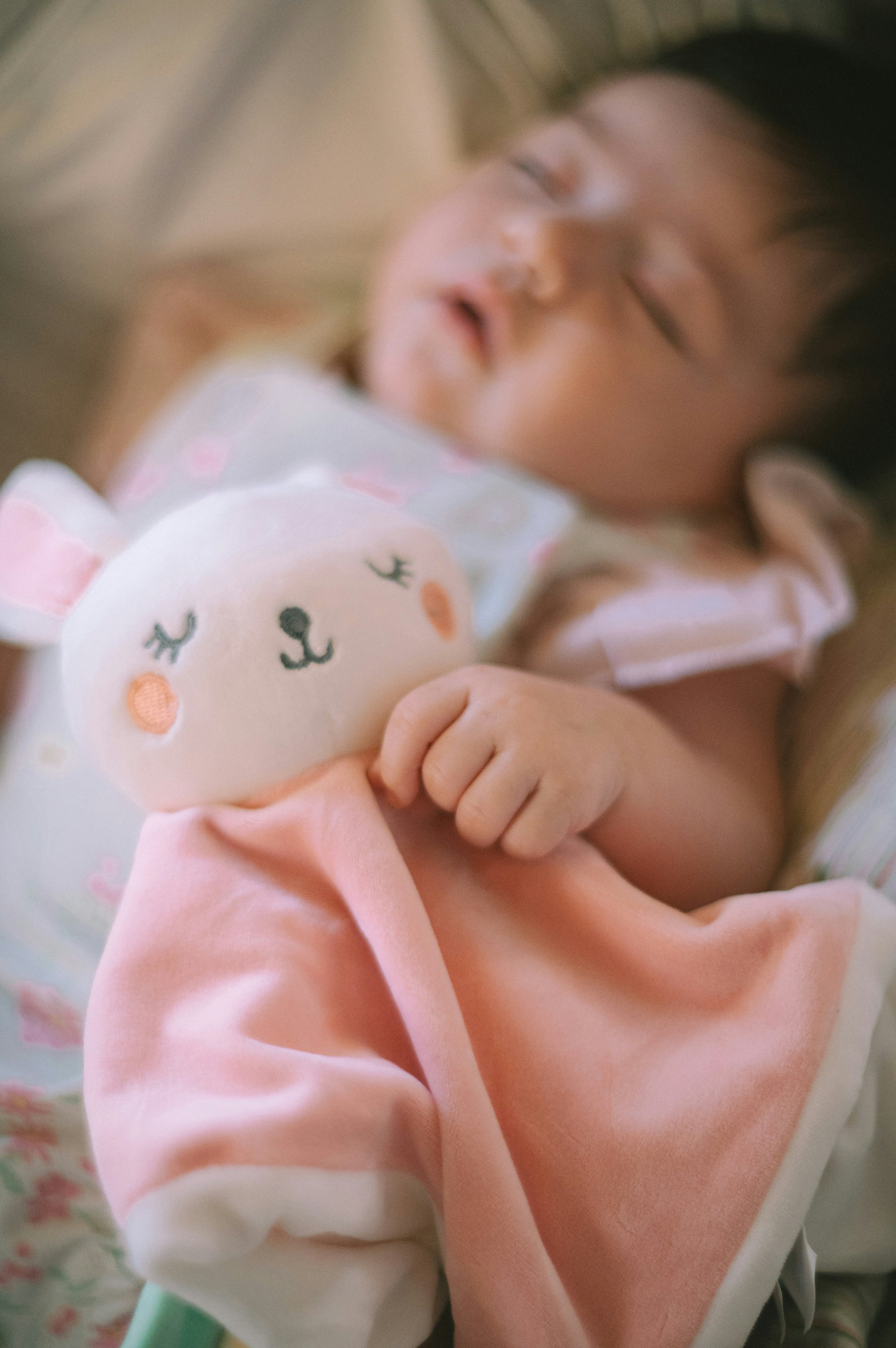 A baby sleeping while holding a soft pink plush rabbit security blanket
