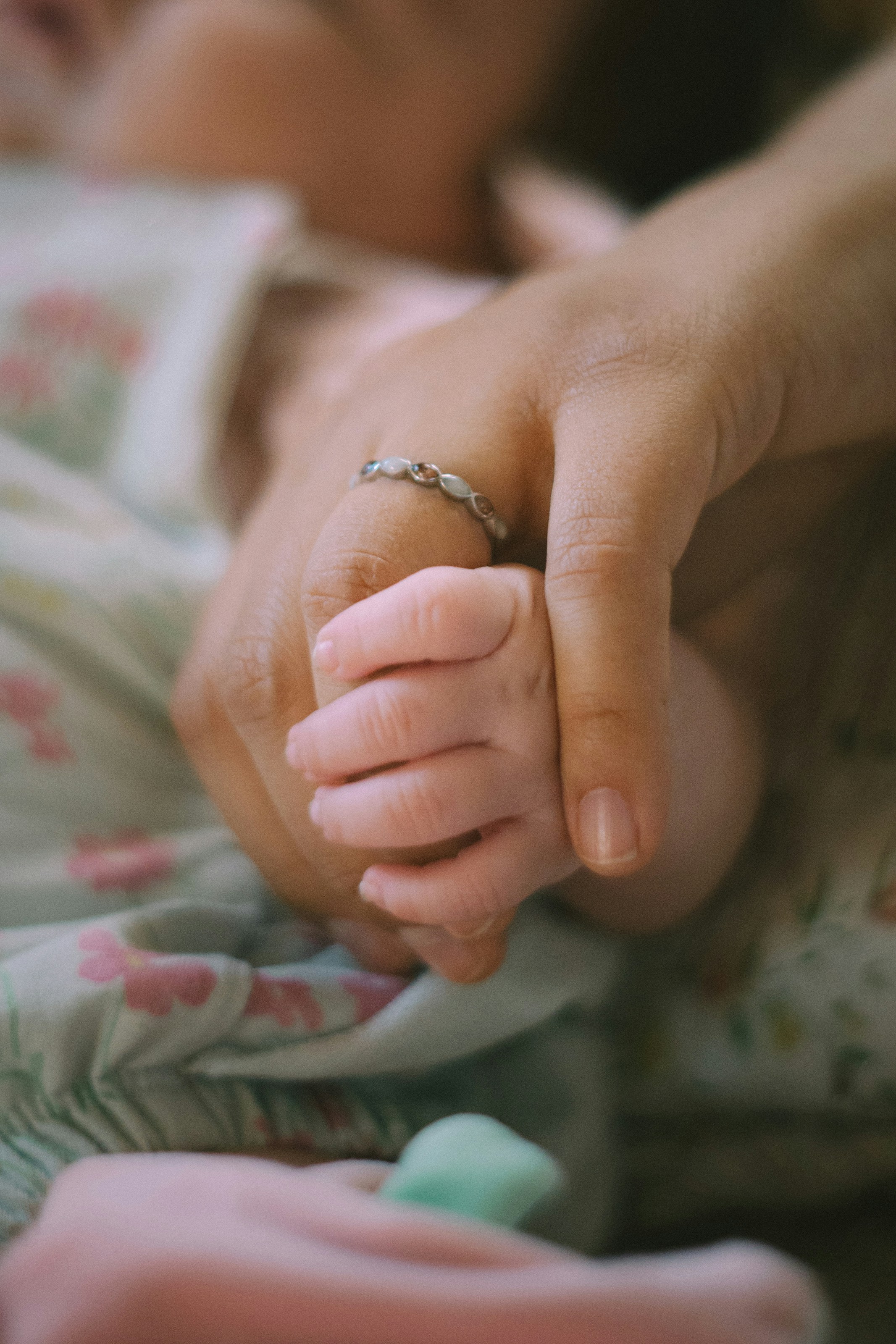 An adult hand wearing a ring holding a baby hand