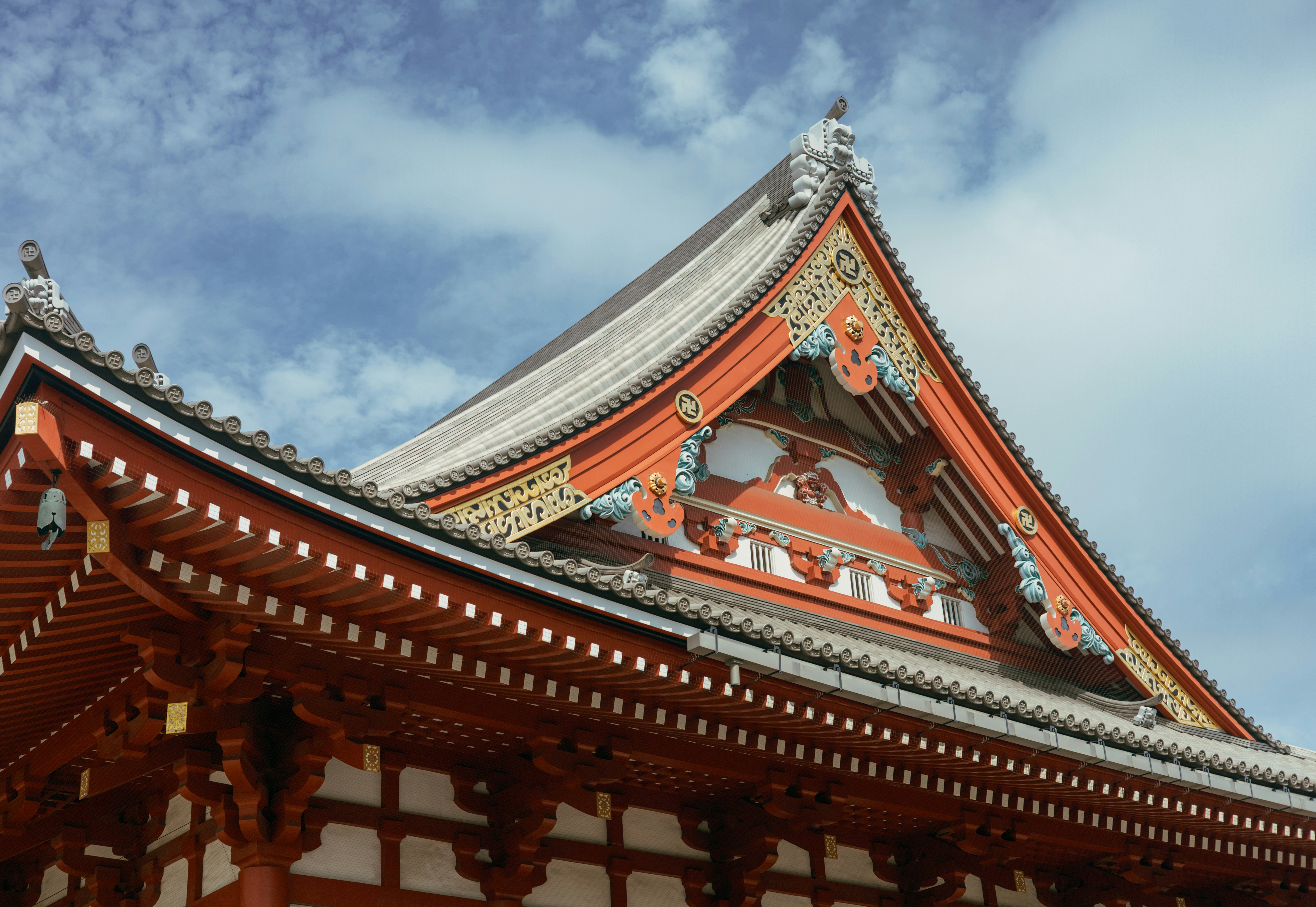 The ornate orange and white gabled roof of a Japanese temple against blue sky