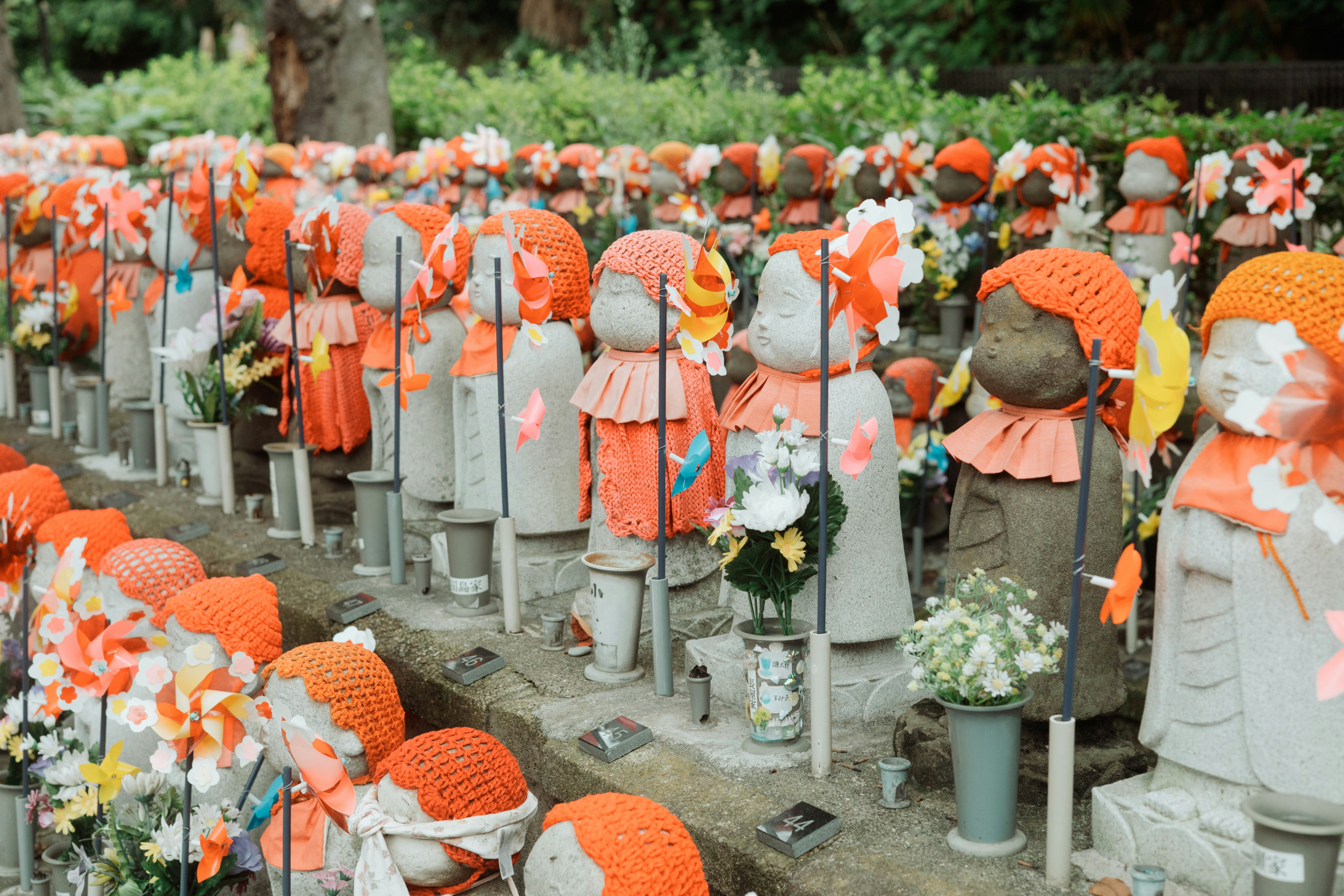 Stone statues wearing orange knitted caps and bibs with colorful pinwheels in a cemetery