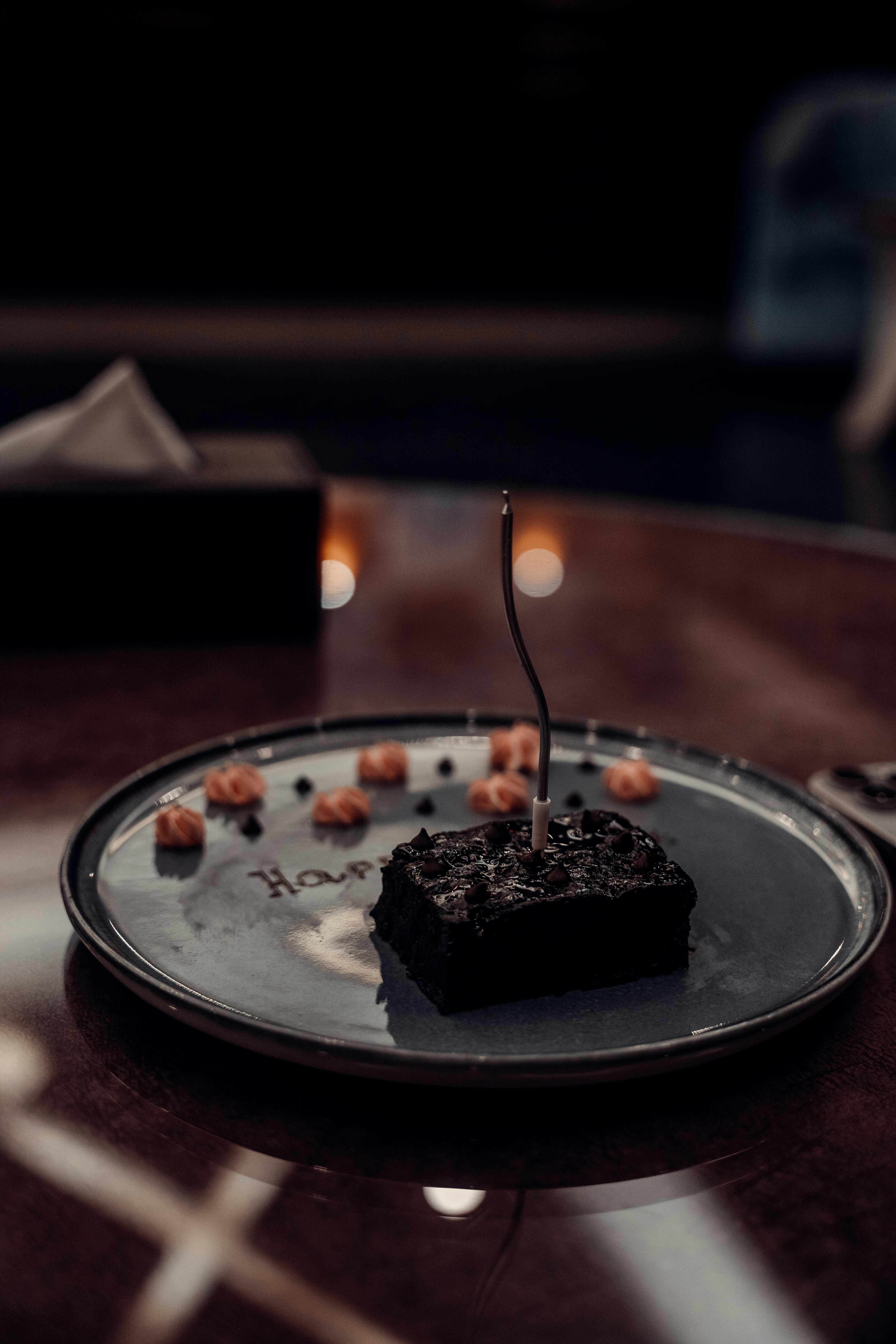 A chocolate brownie with a single candle on a plate with piped frosting