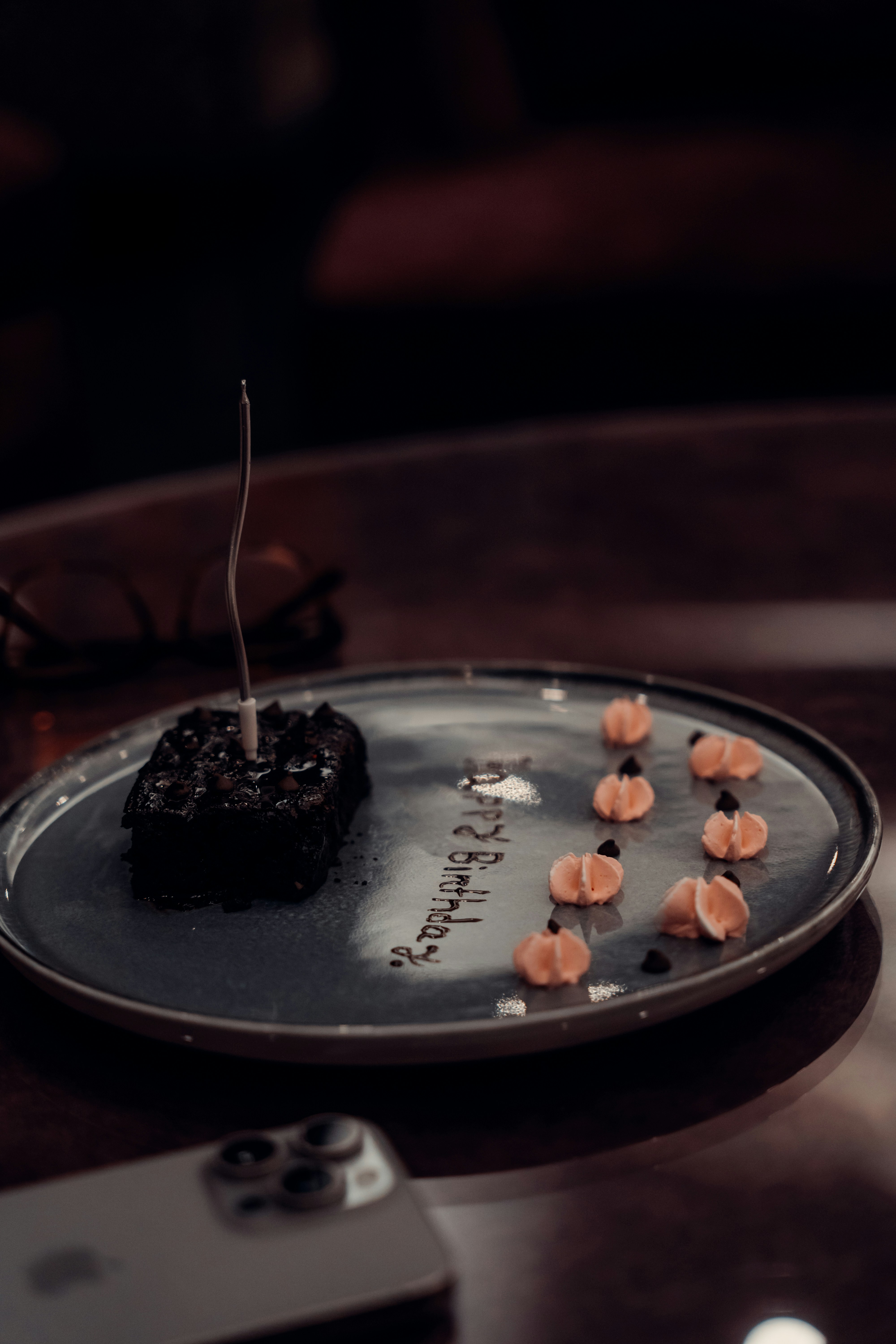 A chocolate brownie with a single candle on a plate with piped frosting