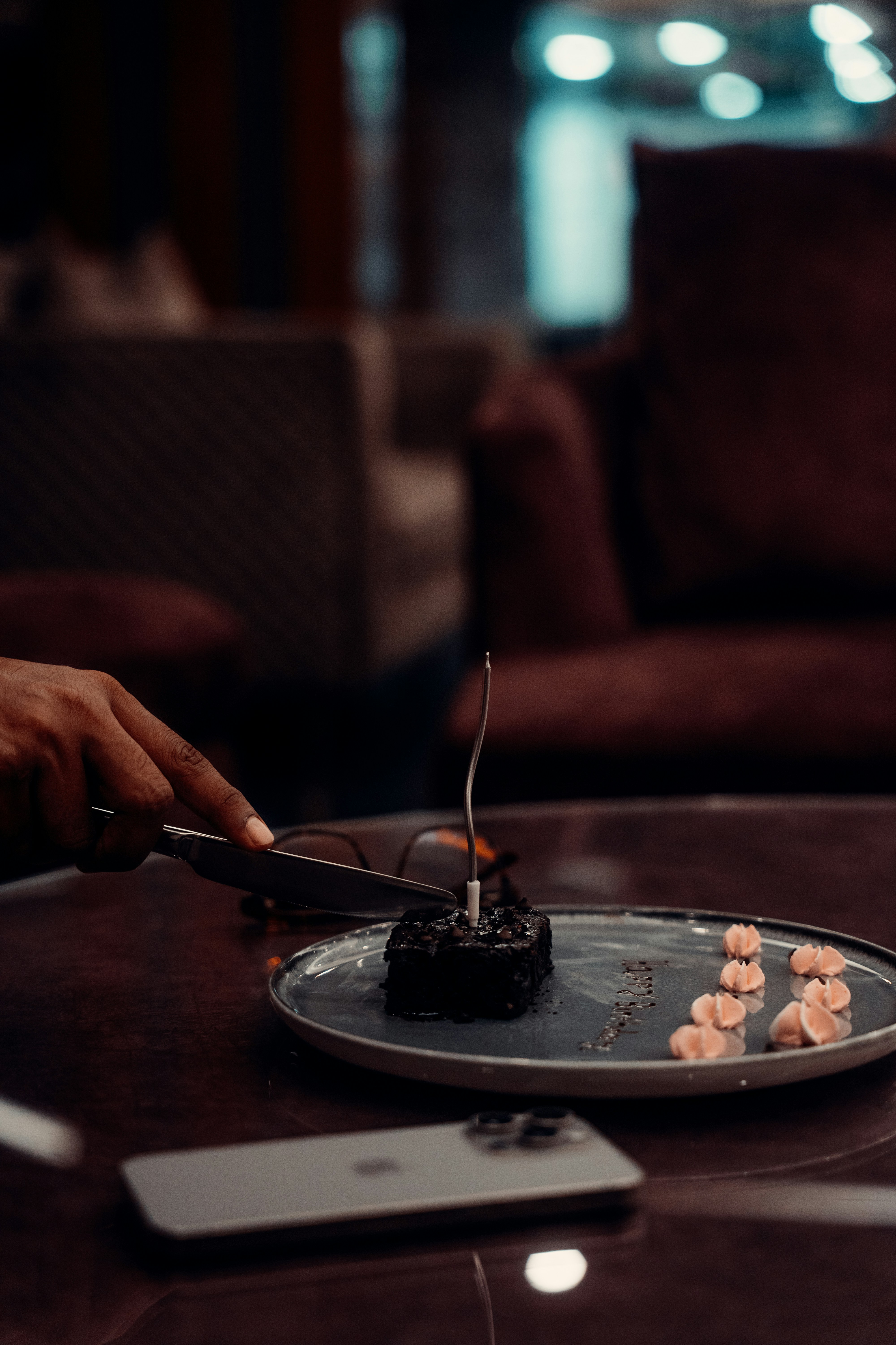 A hand cutting a chocolate brownie with a single candle on a plate
