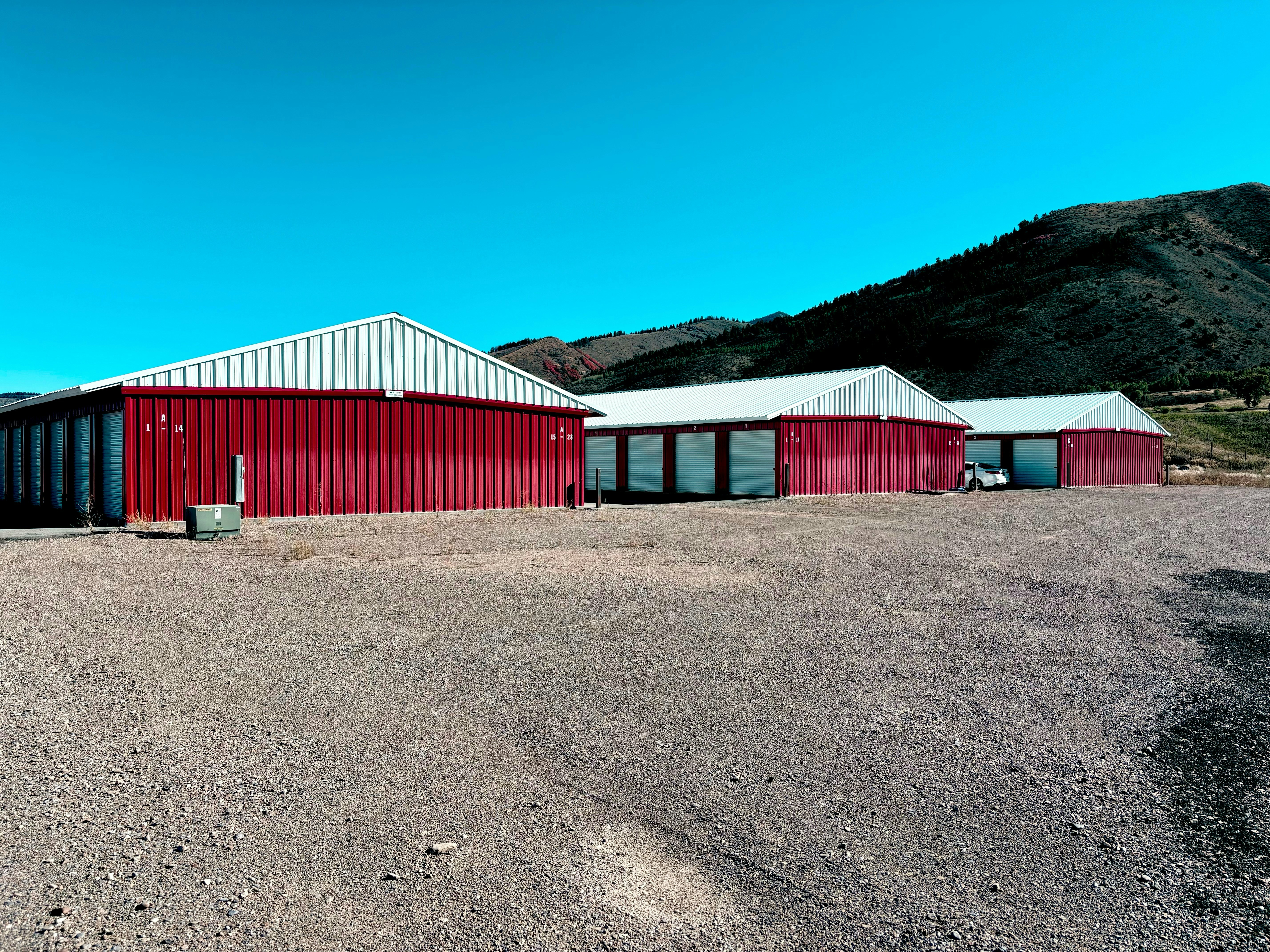 Tres edificios de almacenamiento rojos y blancos en un terreno de grava frente a una montaña