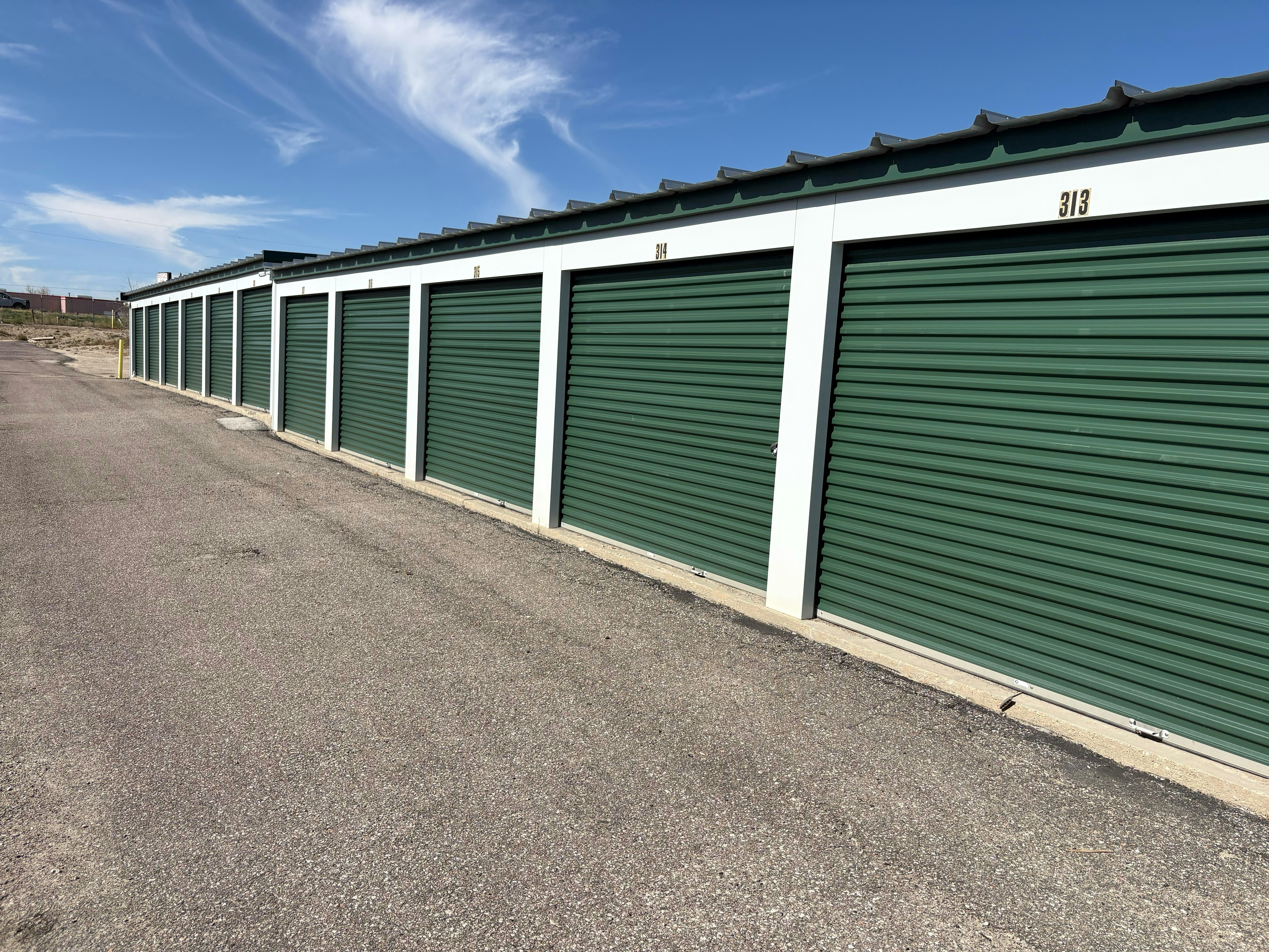 Una fila de puertas metálicas verdes bajo un cielo azul claro