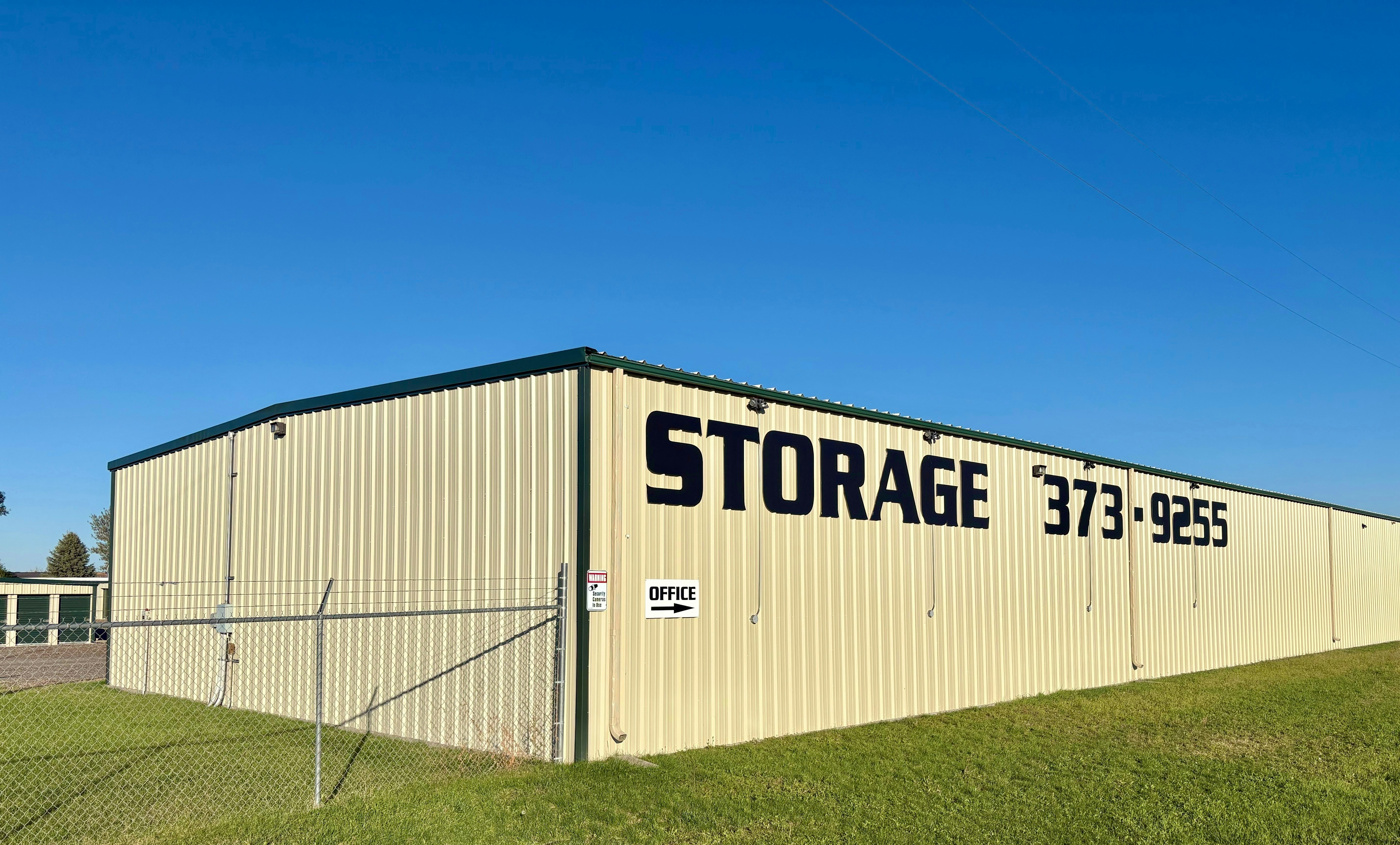 A beige metal storage building with a sign reading STORAGE and a phone number